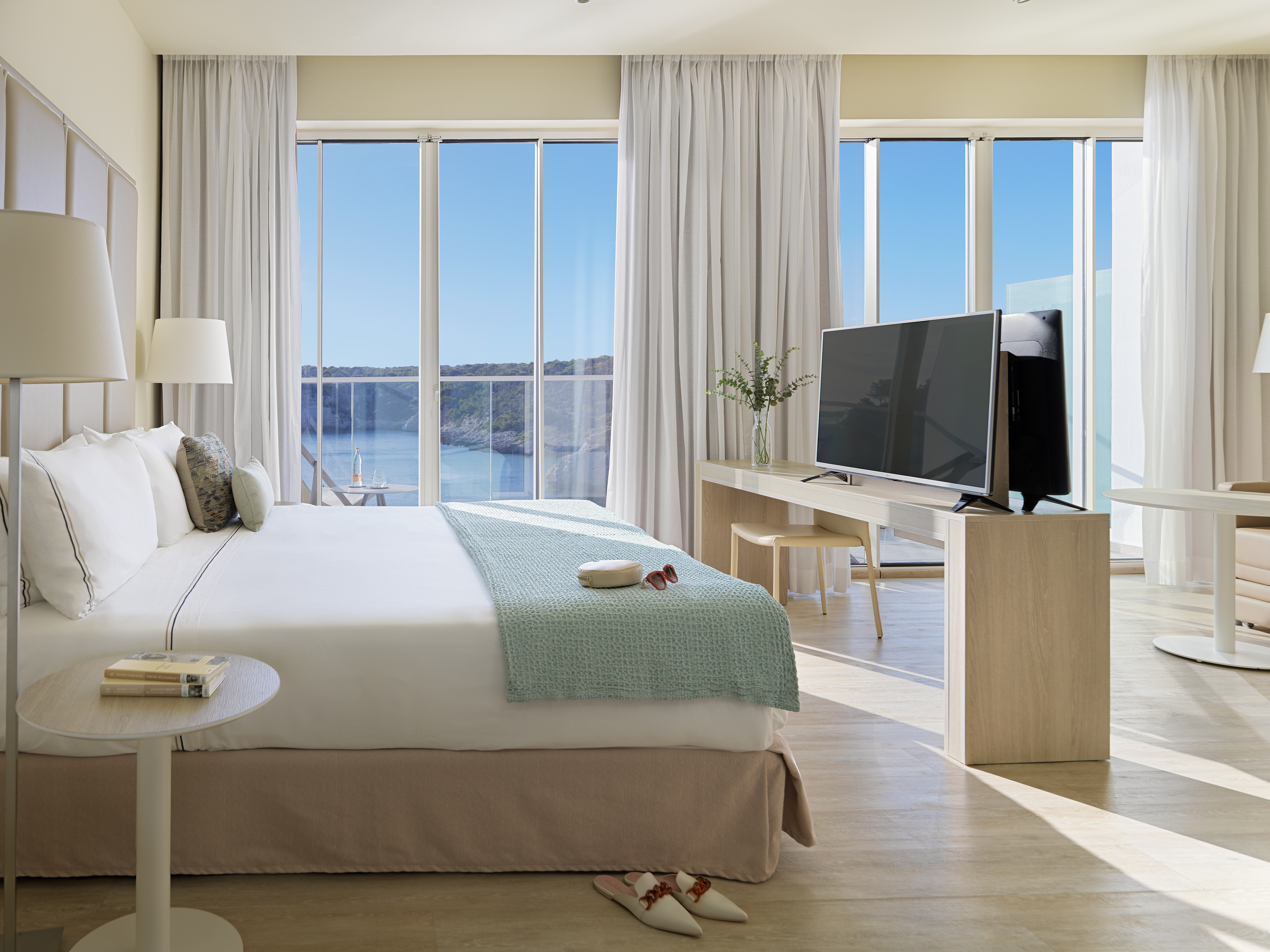 Modern hotel bedroom with panoramic bay views, comfortable bed, and TV.