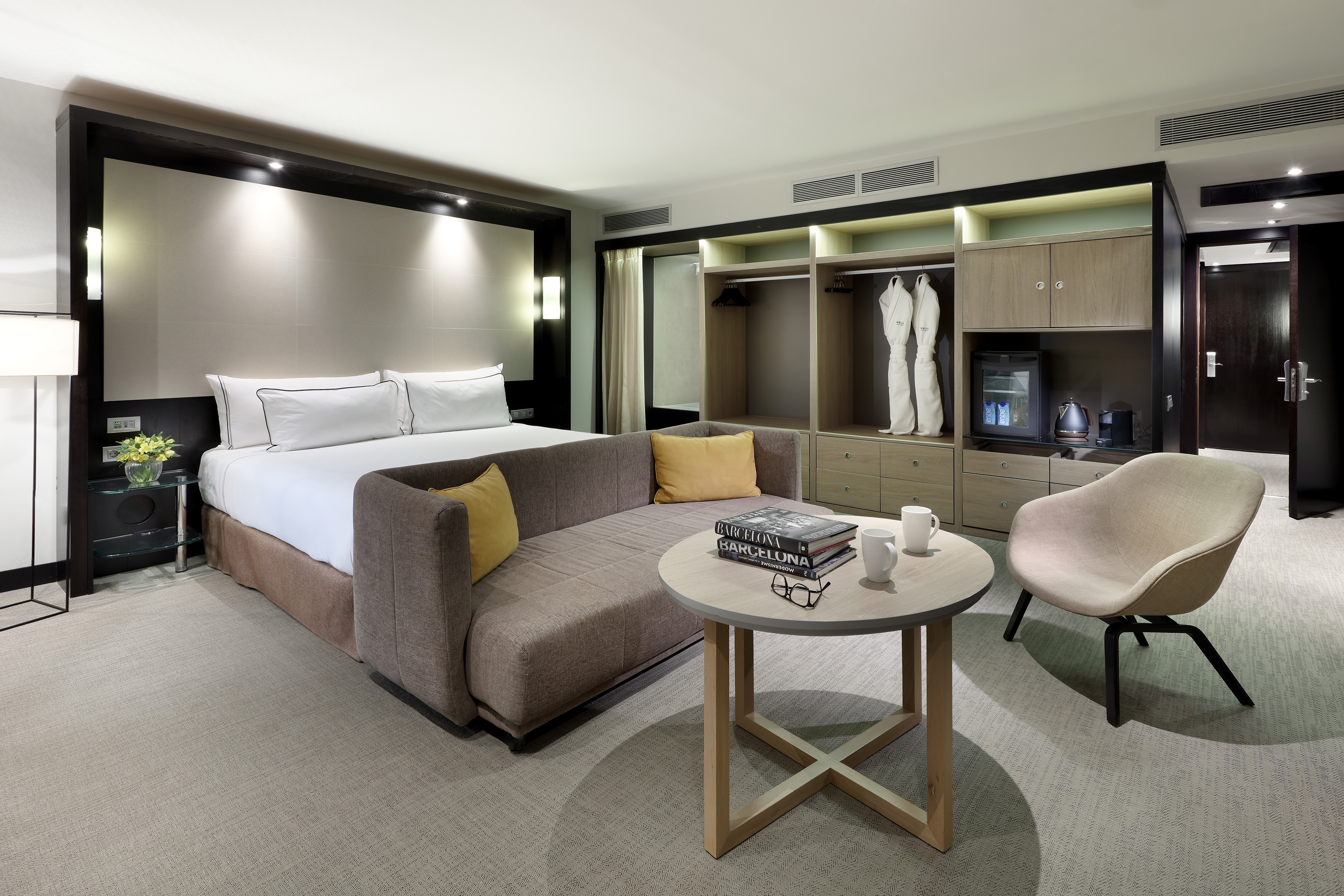Contemporary hotel bedroom with bed, sofa, coffee table, and built-in mini-bar.