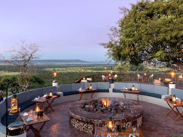 a fire pit with tables and chairs on a patio overlooking a landscape