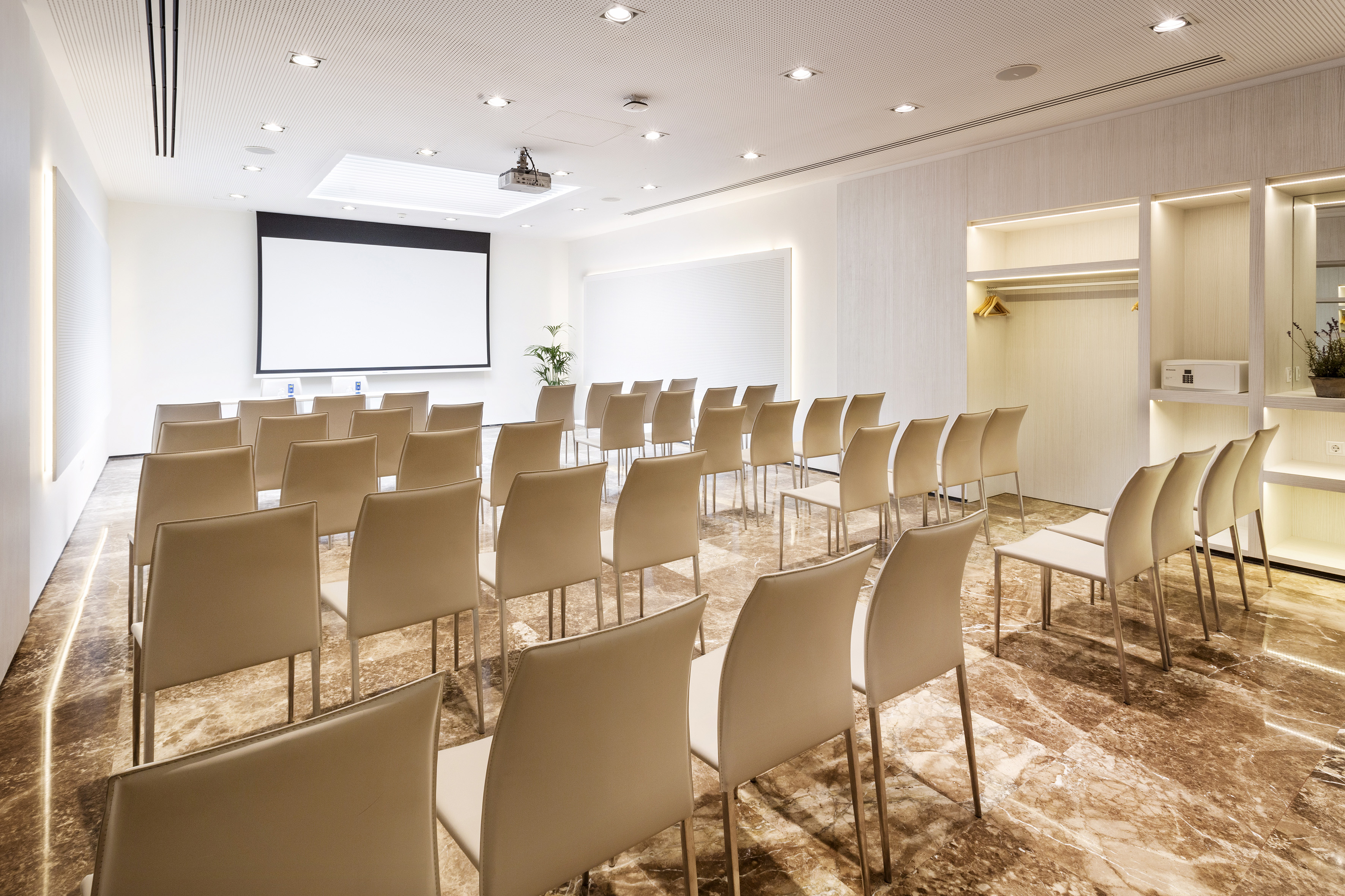 Modern conference room with rows of beige chairs, projector screen, and marble floor.