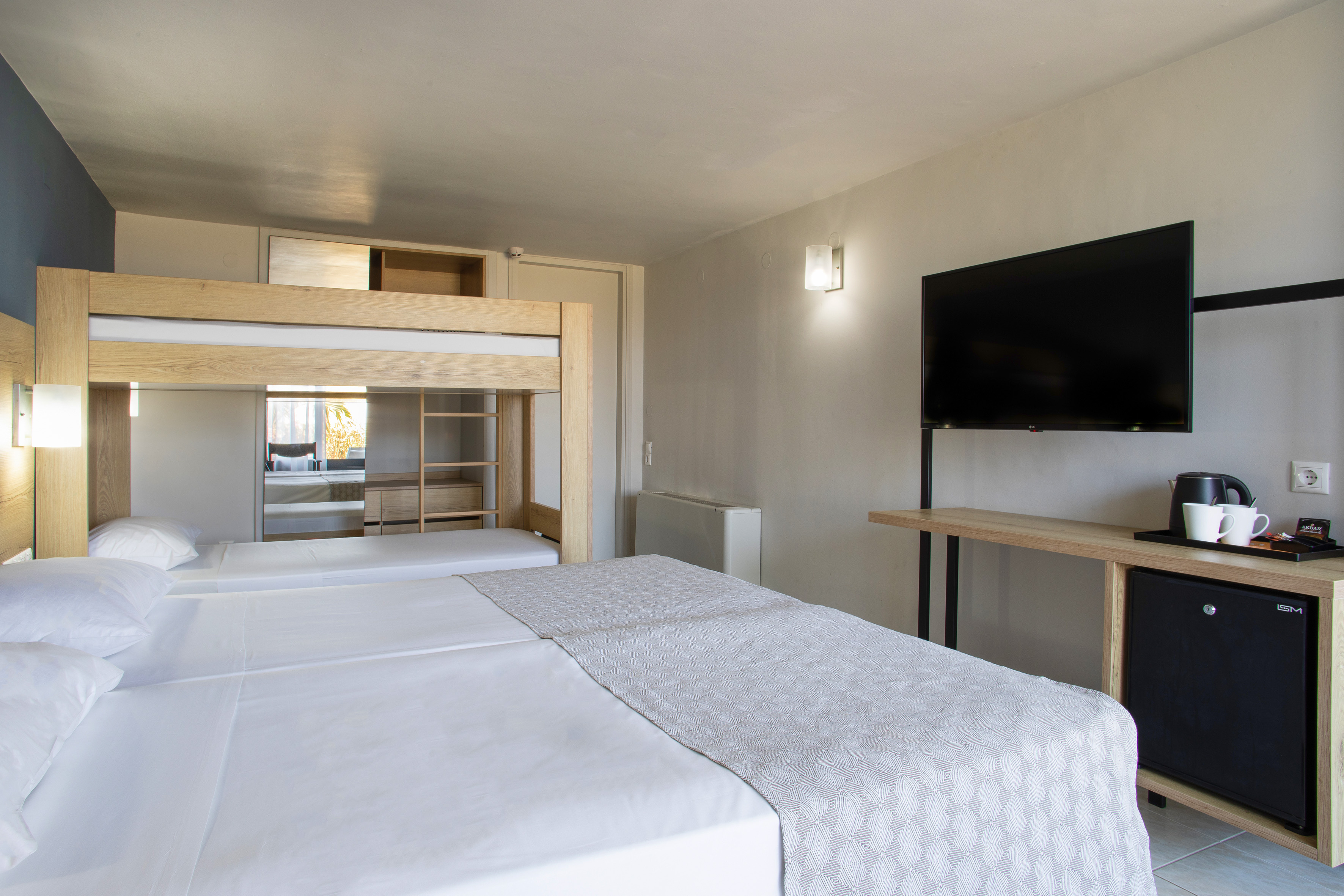 Modern hotel room with bunk beds, twin beds, TV, and mini-fridge.