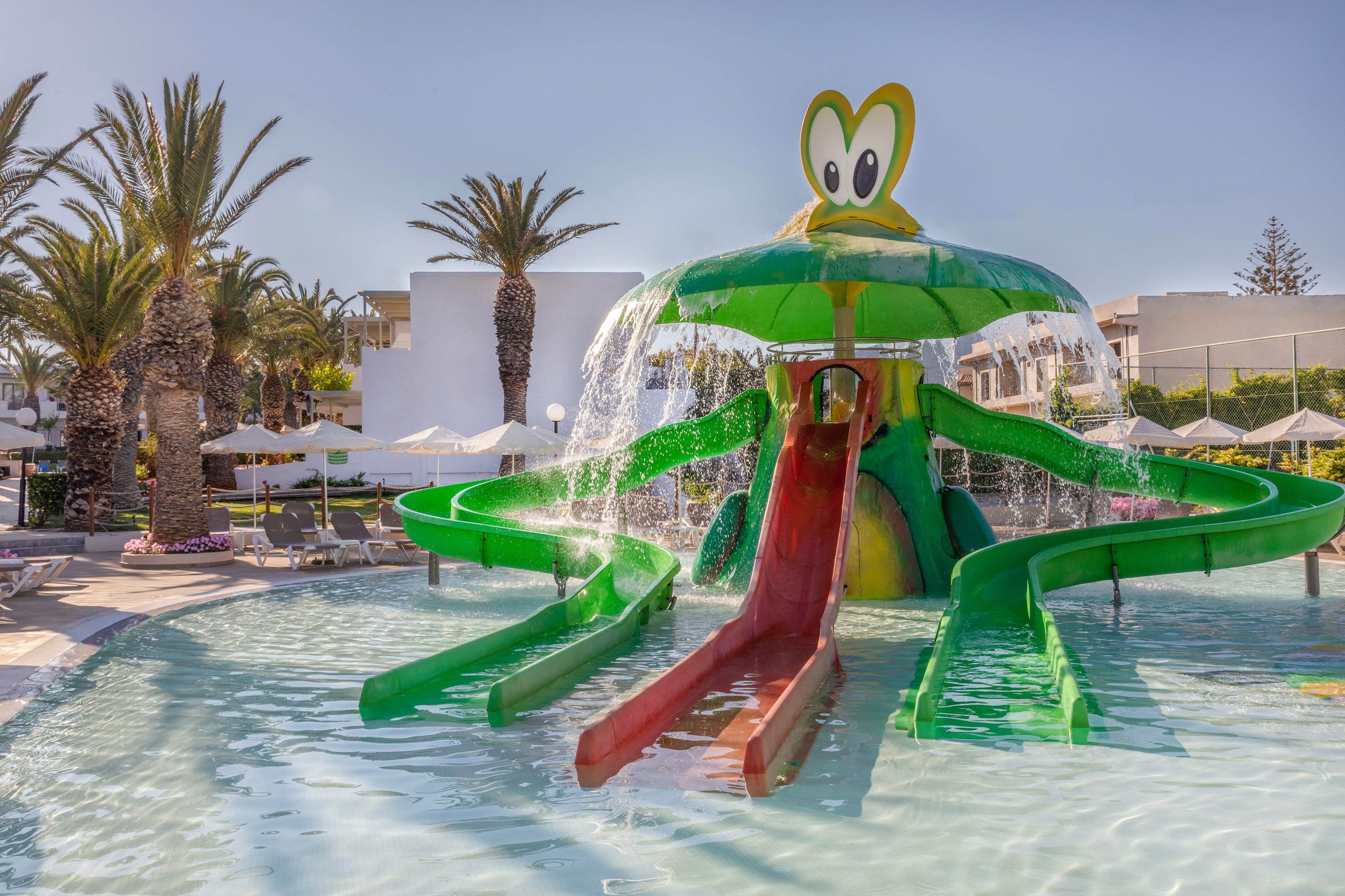 Resort water park with frog-themed slides, palm trees, and a shallow pool.
