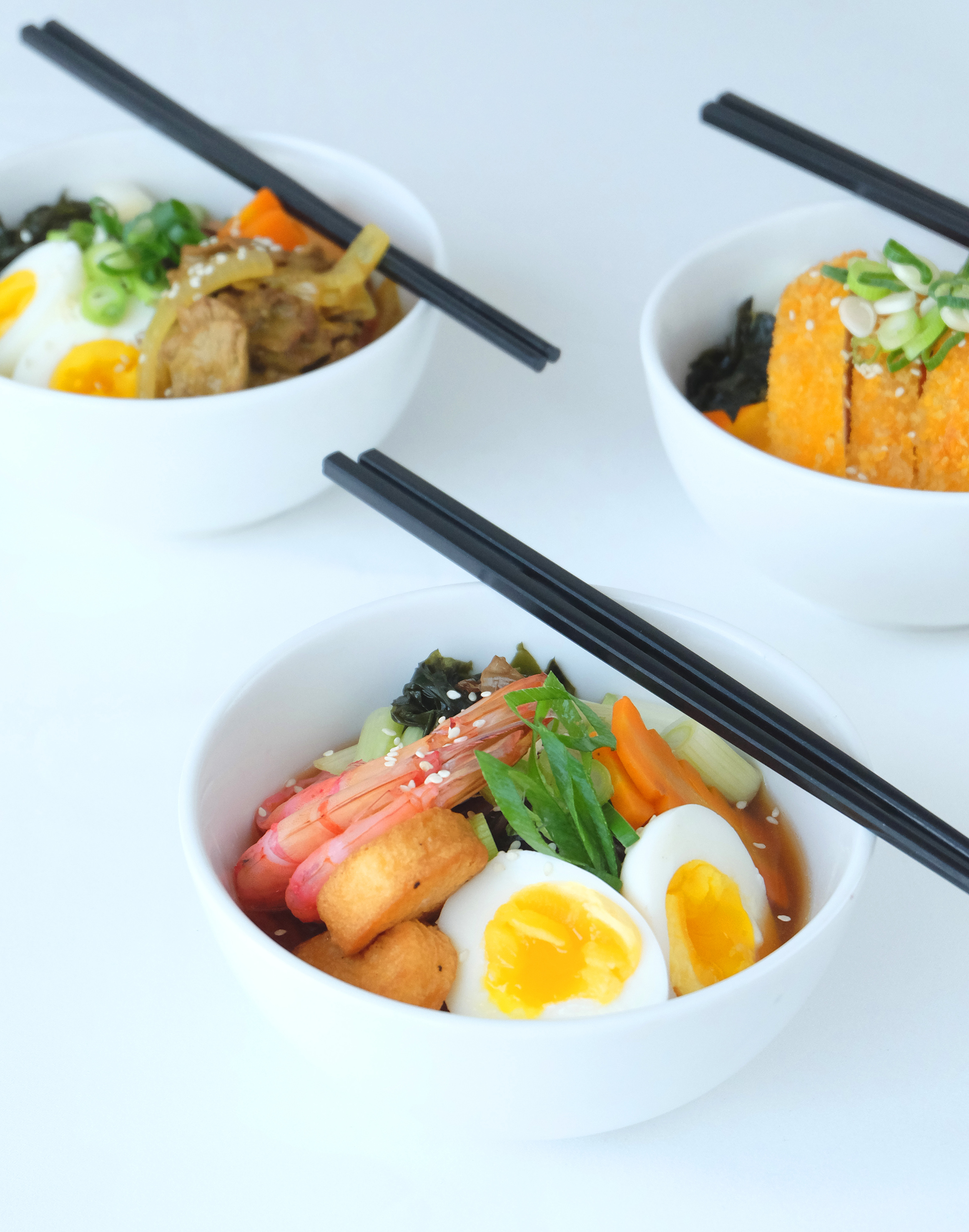 Assorted Asian food bowls: ramen, rice, and katsu with eggs and chopsticks.