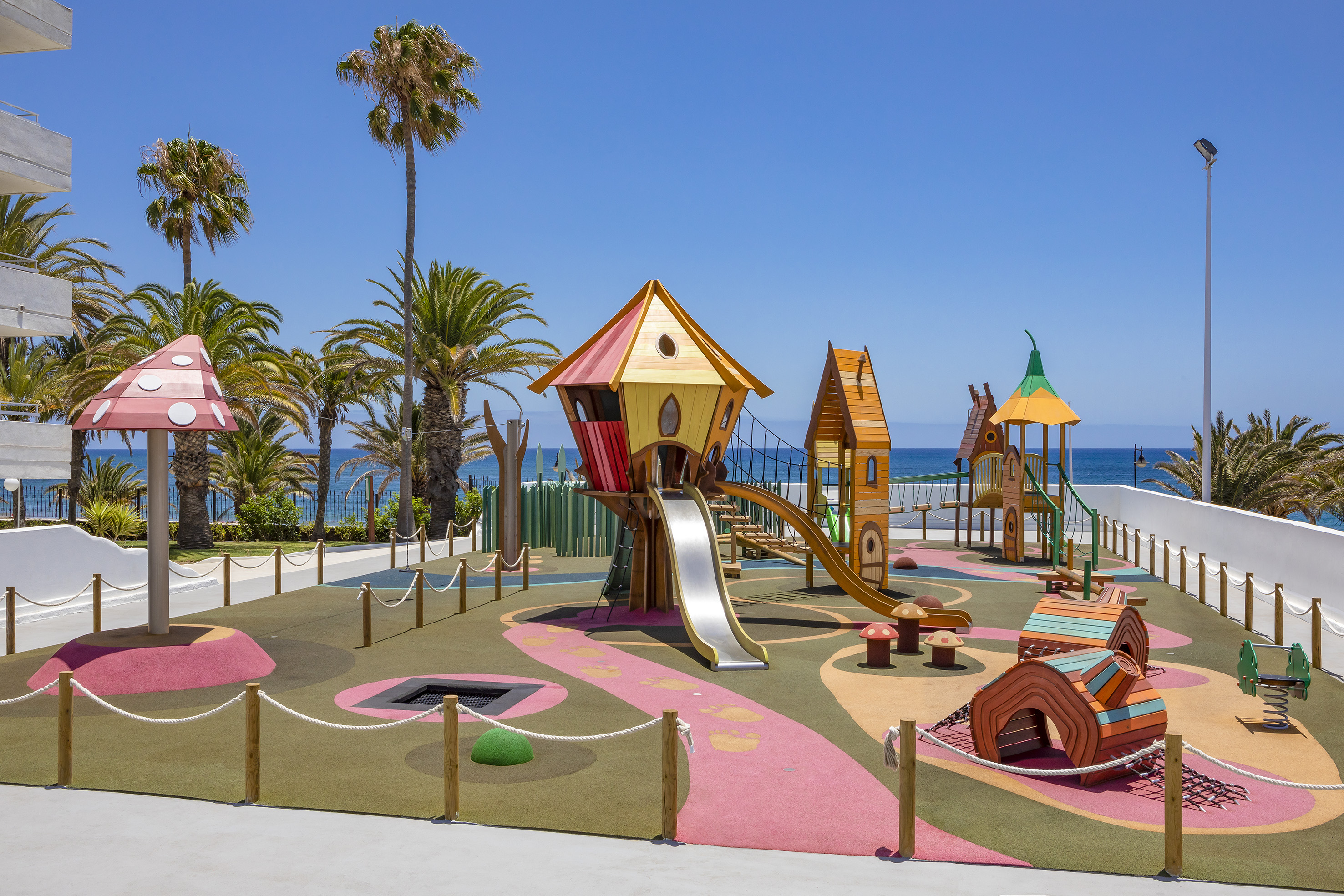 Tropical resort playground with treehouse, slides, palm trees, and ocean view.