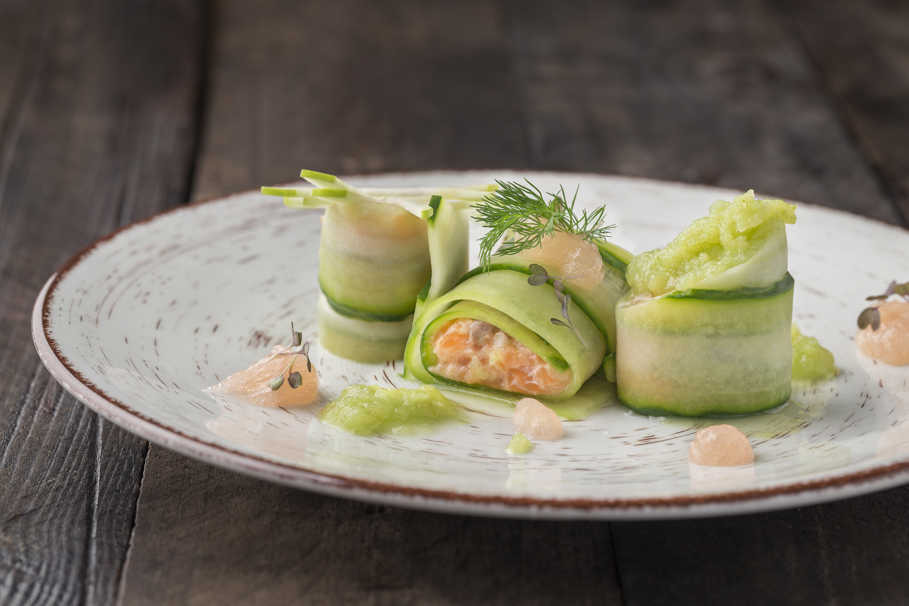 Cucumber salmon rolls appetizer, garnished with dill and grapefruit on a plate.