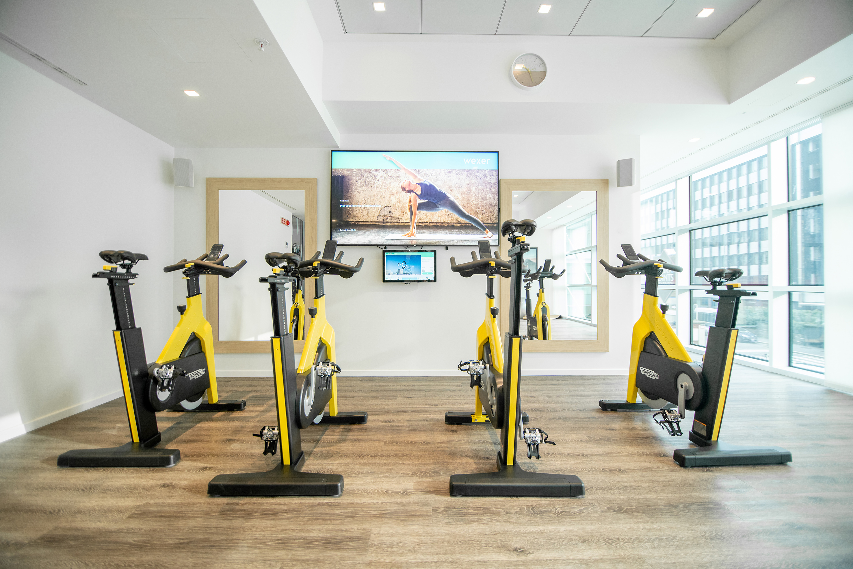 Modern spin studio with five yellow Technogym bikes and screens for virtual workouts.
