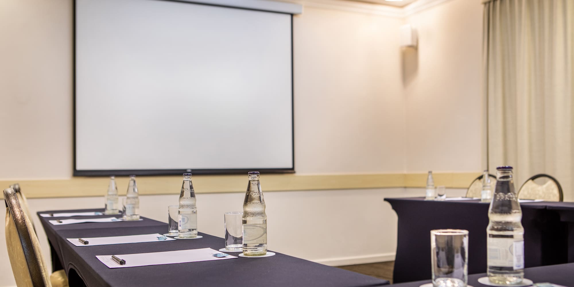 a room with a projection screen and tables with water bottles and glasses