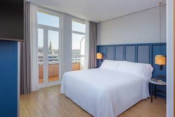 a bed with white sheets and a blue headboard in a room with windows