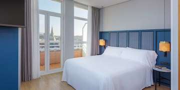 a bed with white sheets and a blue headboard in a room with windows