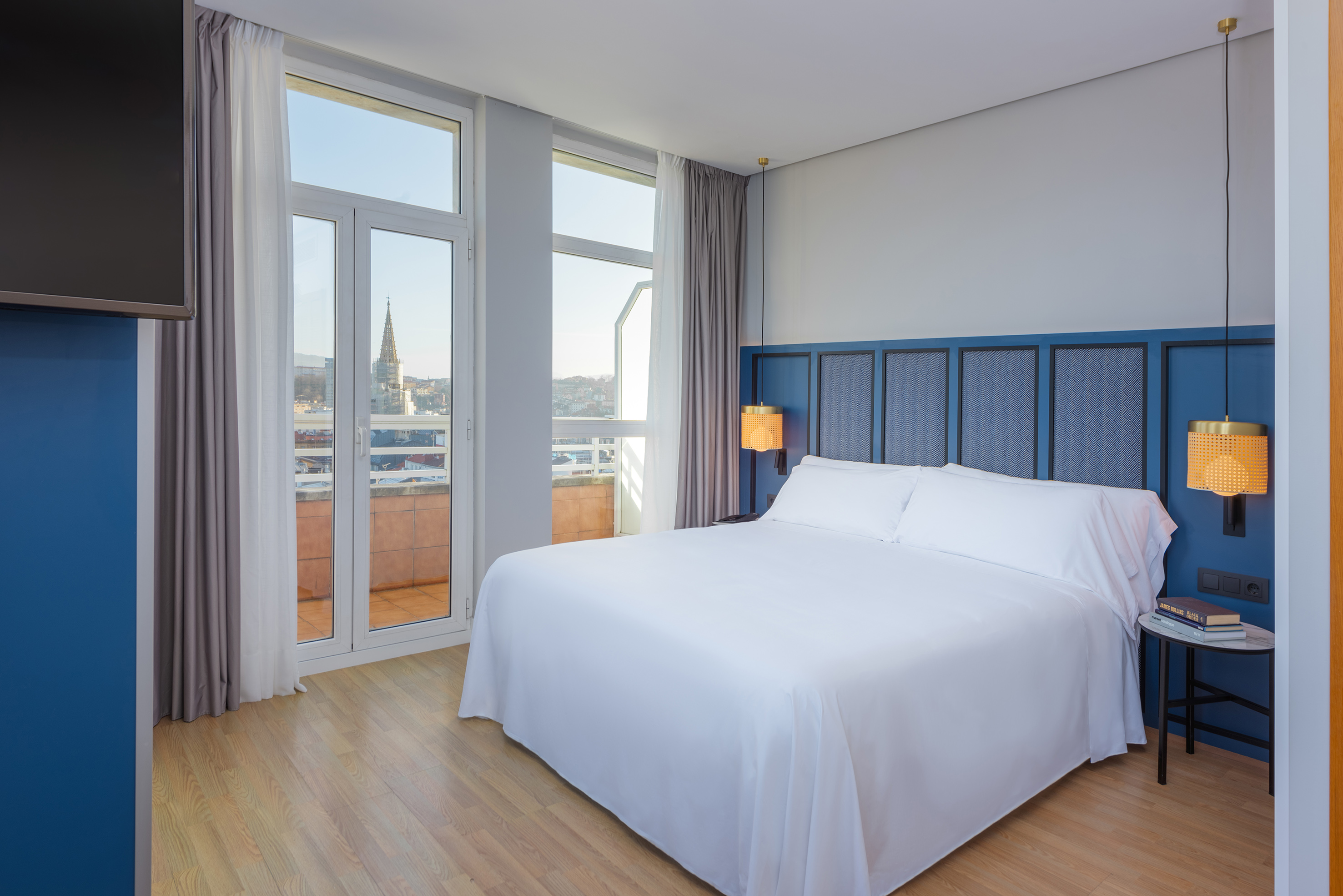 a bed with white sheets and a blue headboard in a room with windows