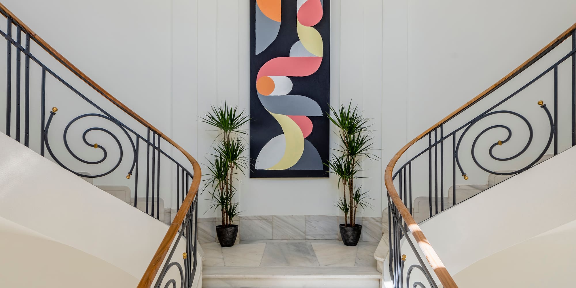 Elegant marble split staircase, ornate wrought iron balustrade, colorful abstract art.