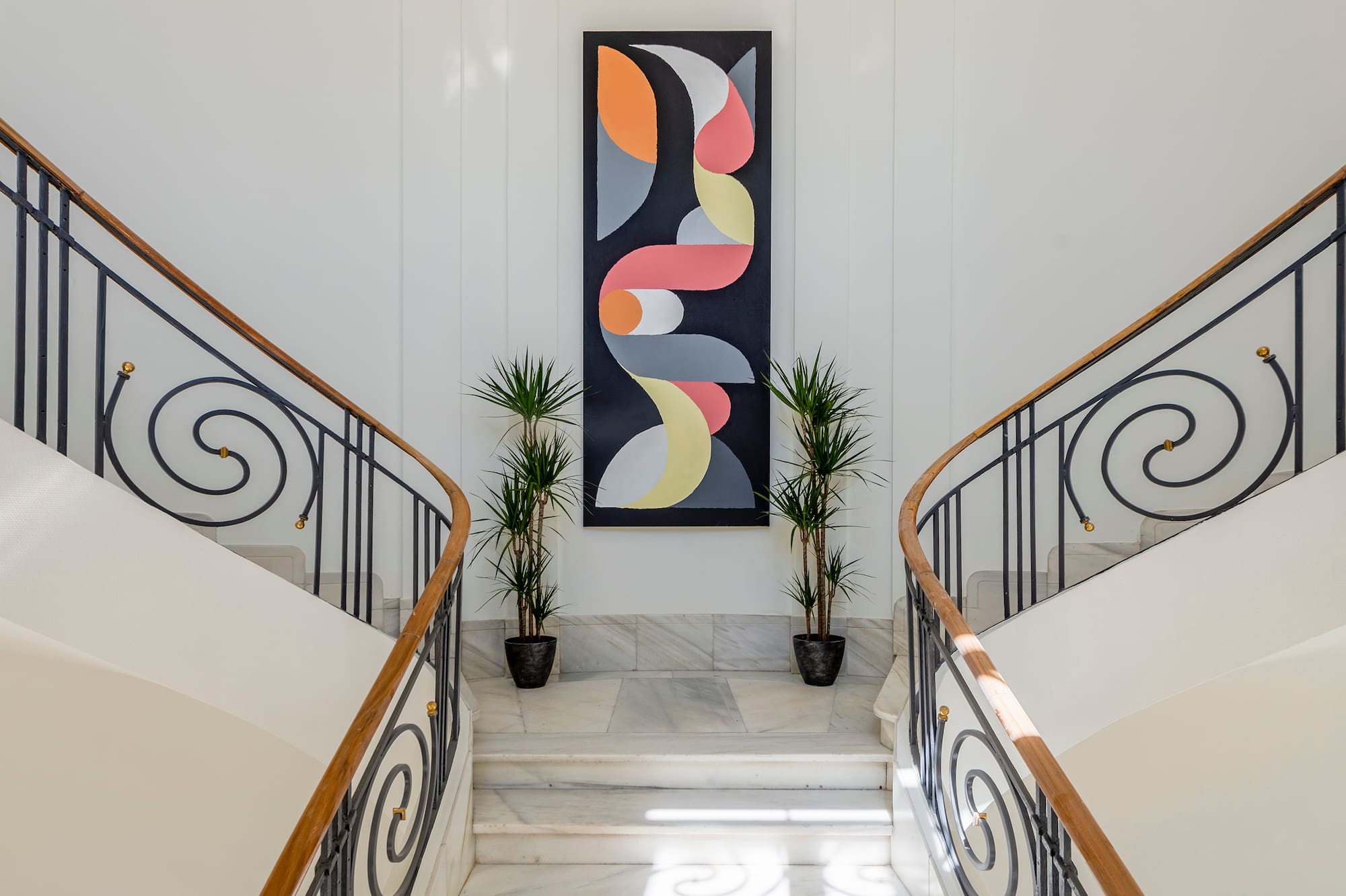 Foyer with split marble staircase, wrought iron, abstract art, and plants.