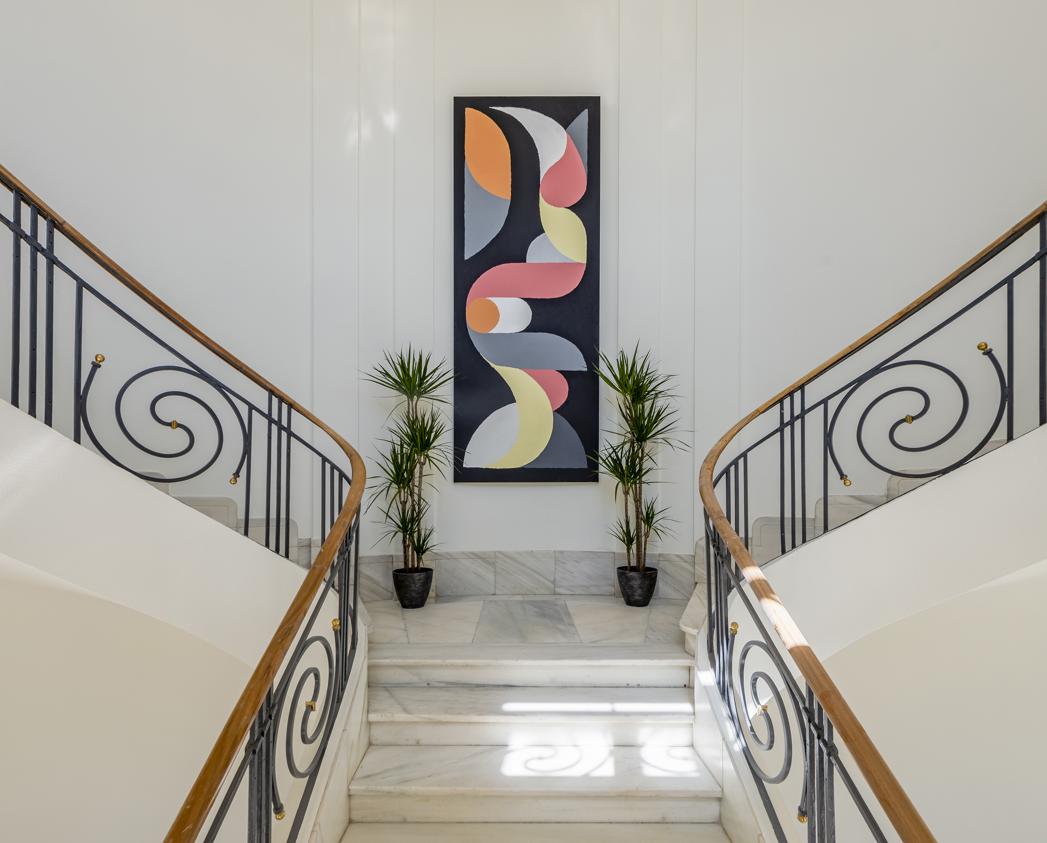 Elegant marble split staircase, ornate wrought iron balustrade, colorful abstract art.