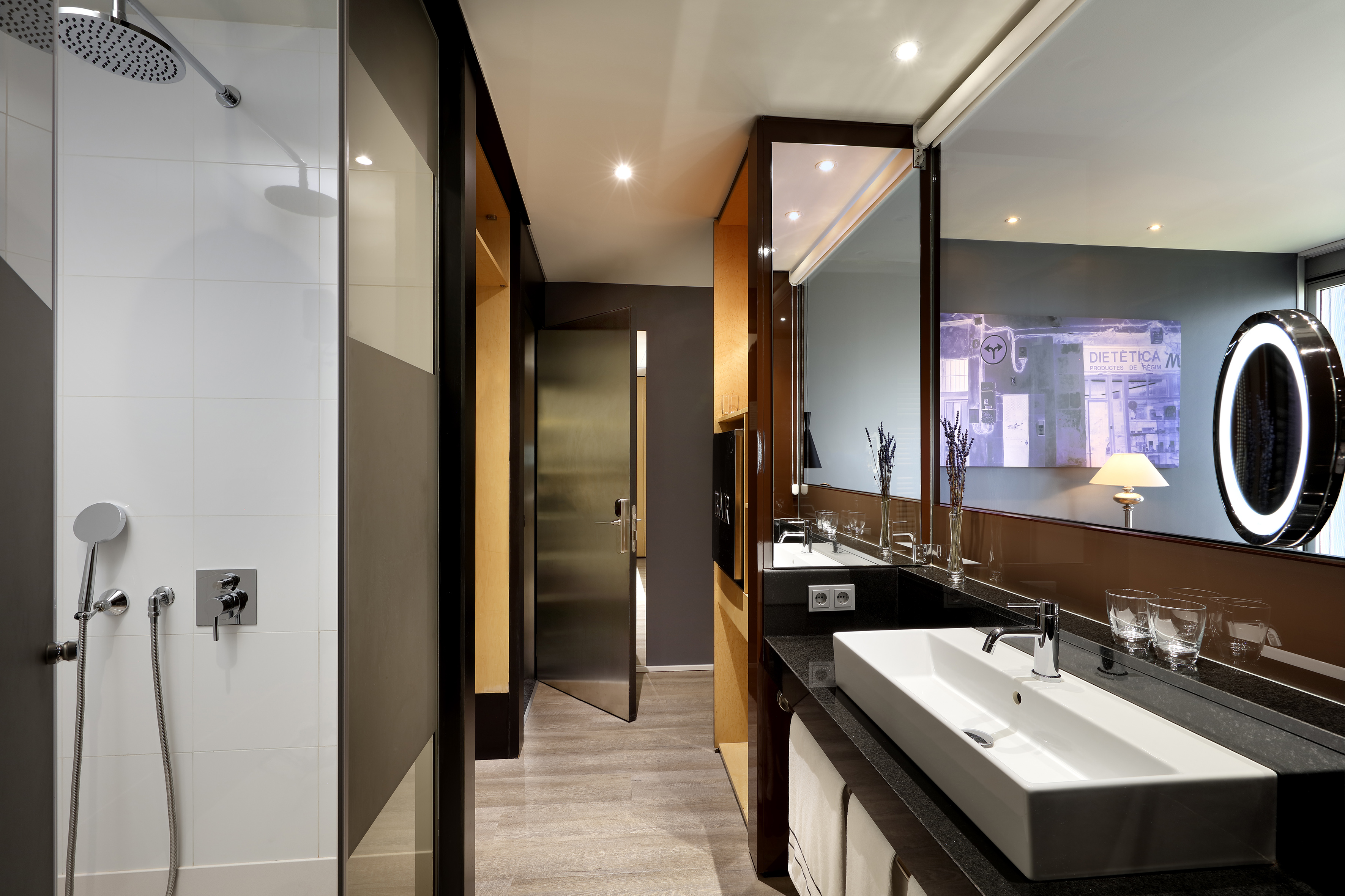Modern hotel bathroom with walk-in shower, large vanity, sink, and backlit mirror.