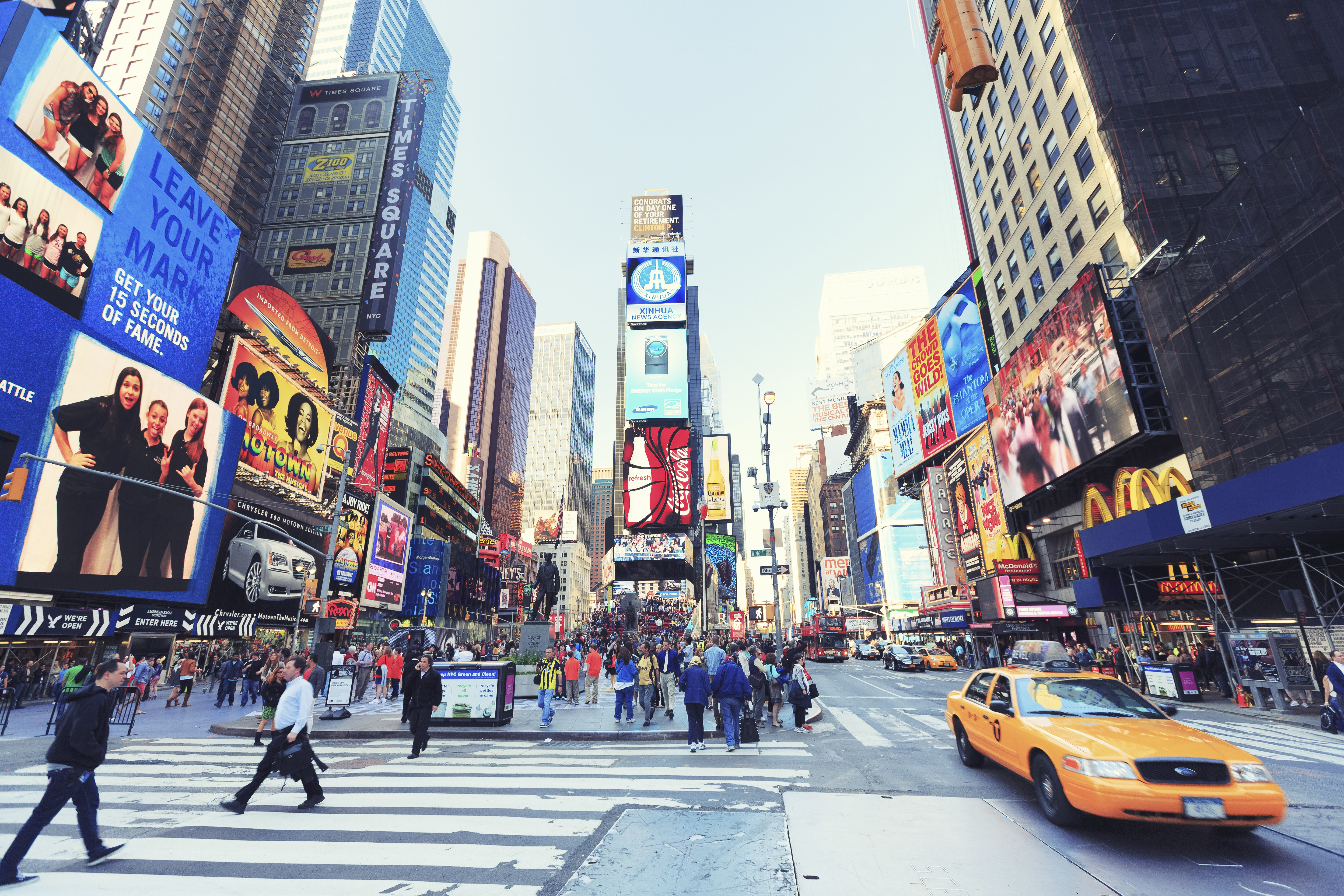 a busy city street with people walking and pedestrians with Times Square in the background