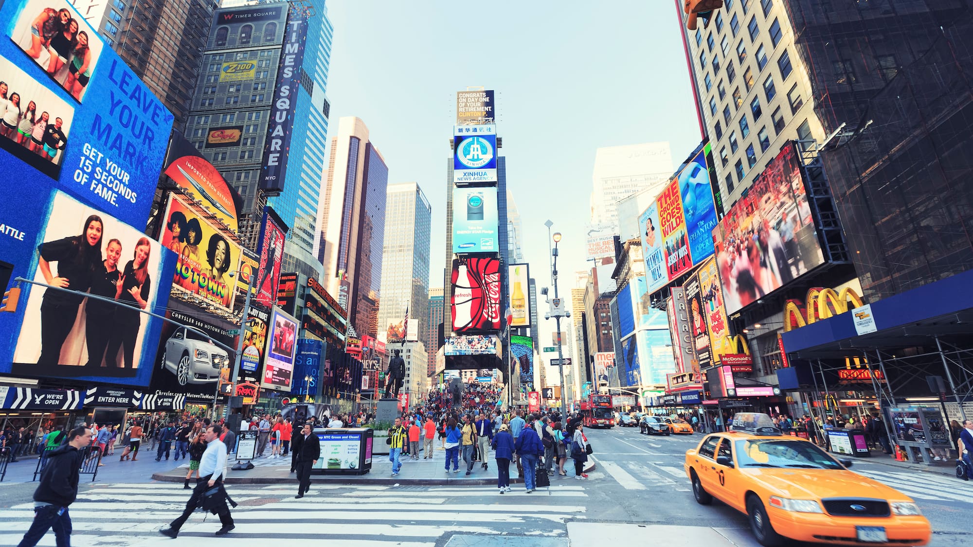 a busy city street with people walking and pedestrians with Times Square in the background