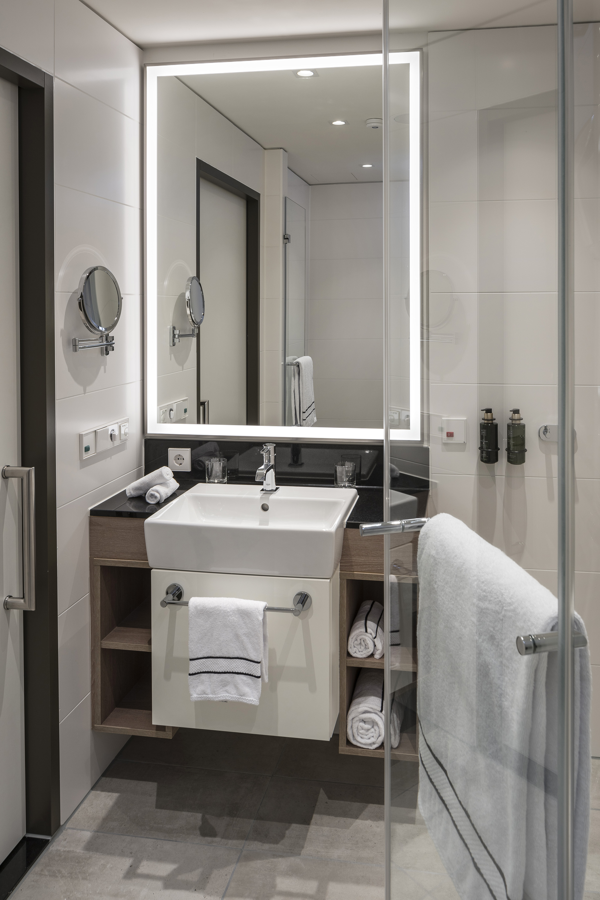 Modern hotel bathroom with white sink, illuminated mirror, and glass shower.