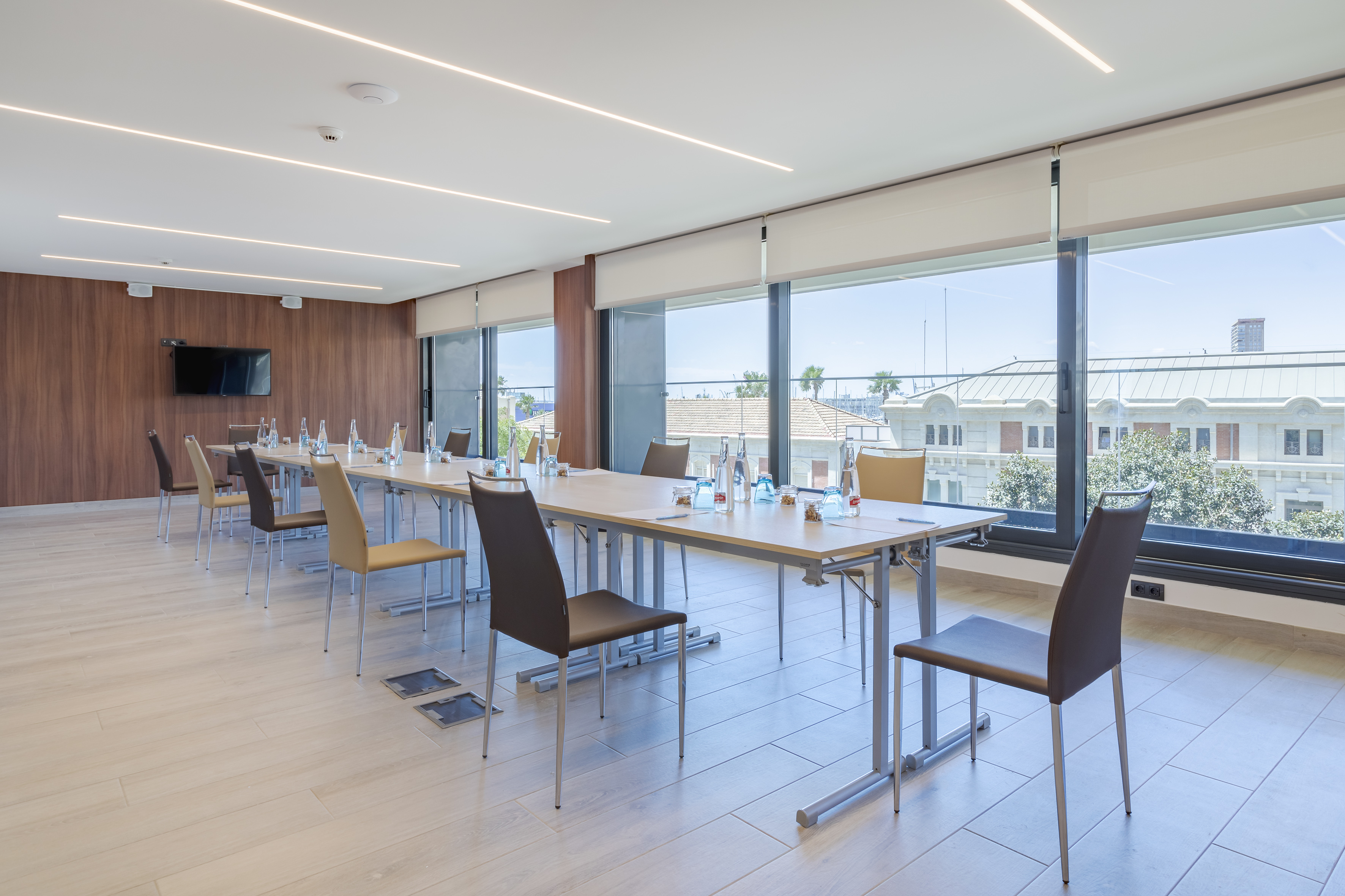 Modern conference room with long table, chairs, natural light, and city view.