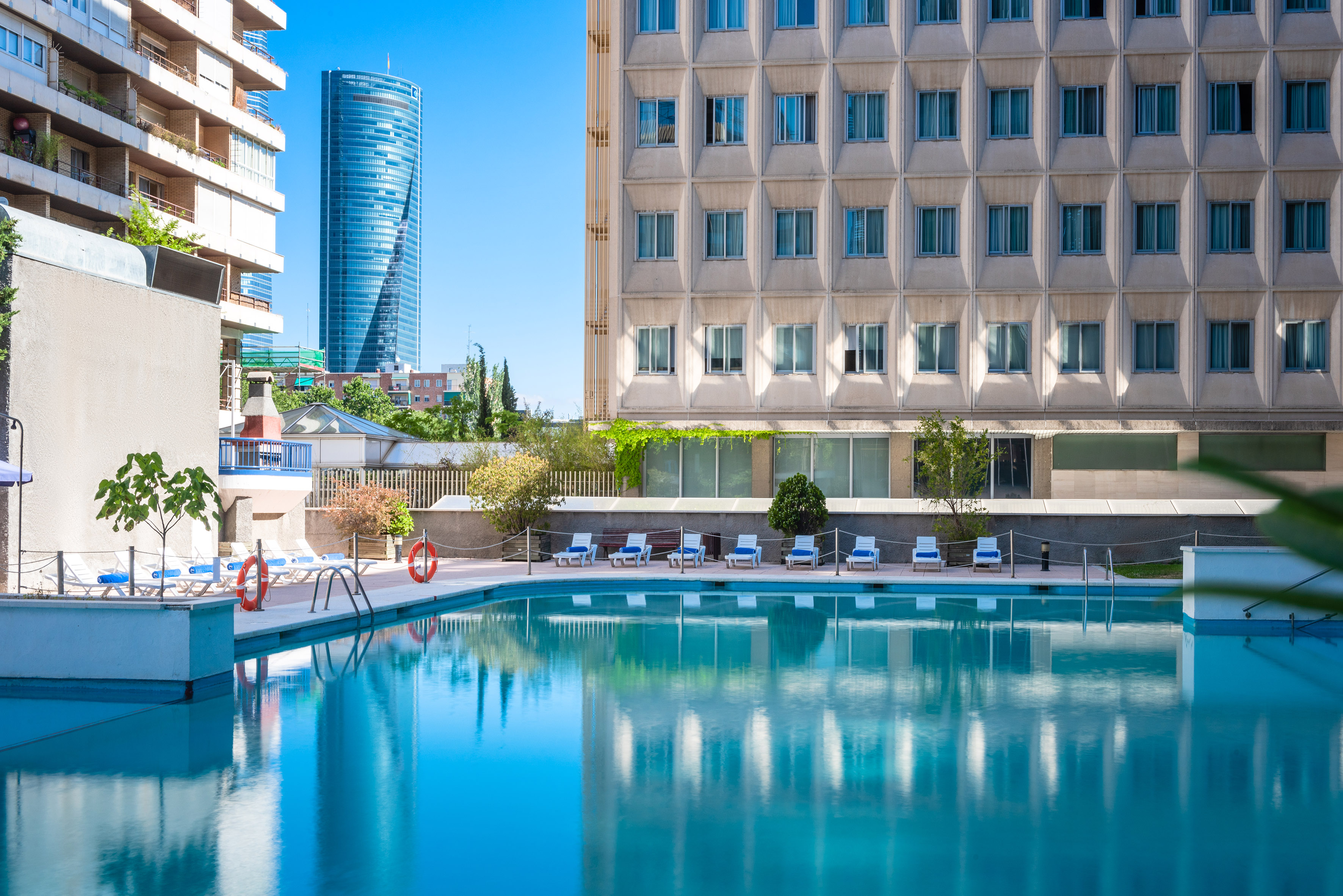 Hotel swimming pool with modern city buildings and a tall glass skyscraper.