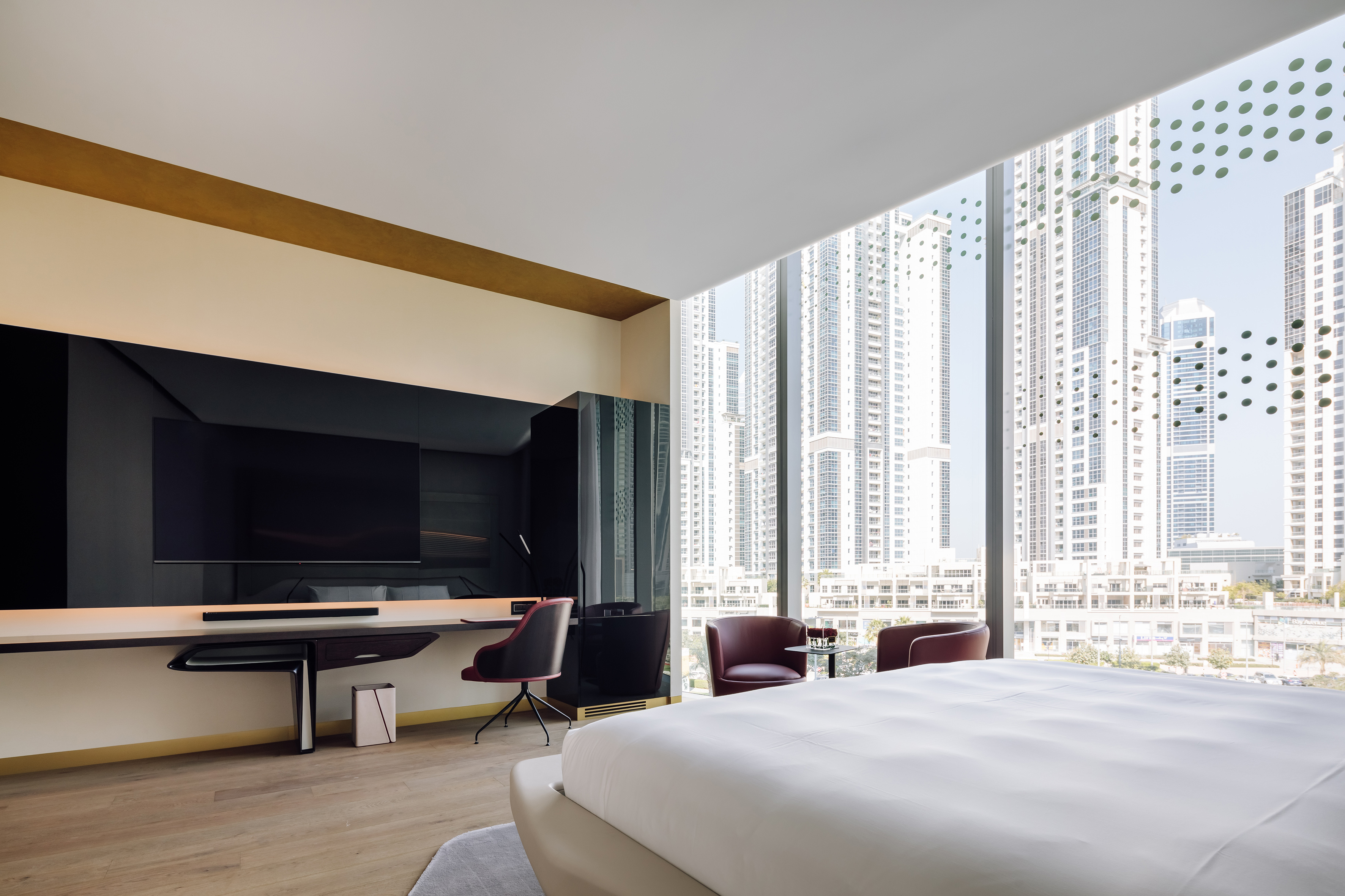 Modern hotel bedroom with city skyline view, large bed, and work desk.