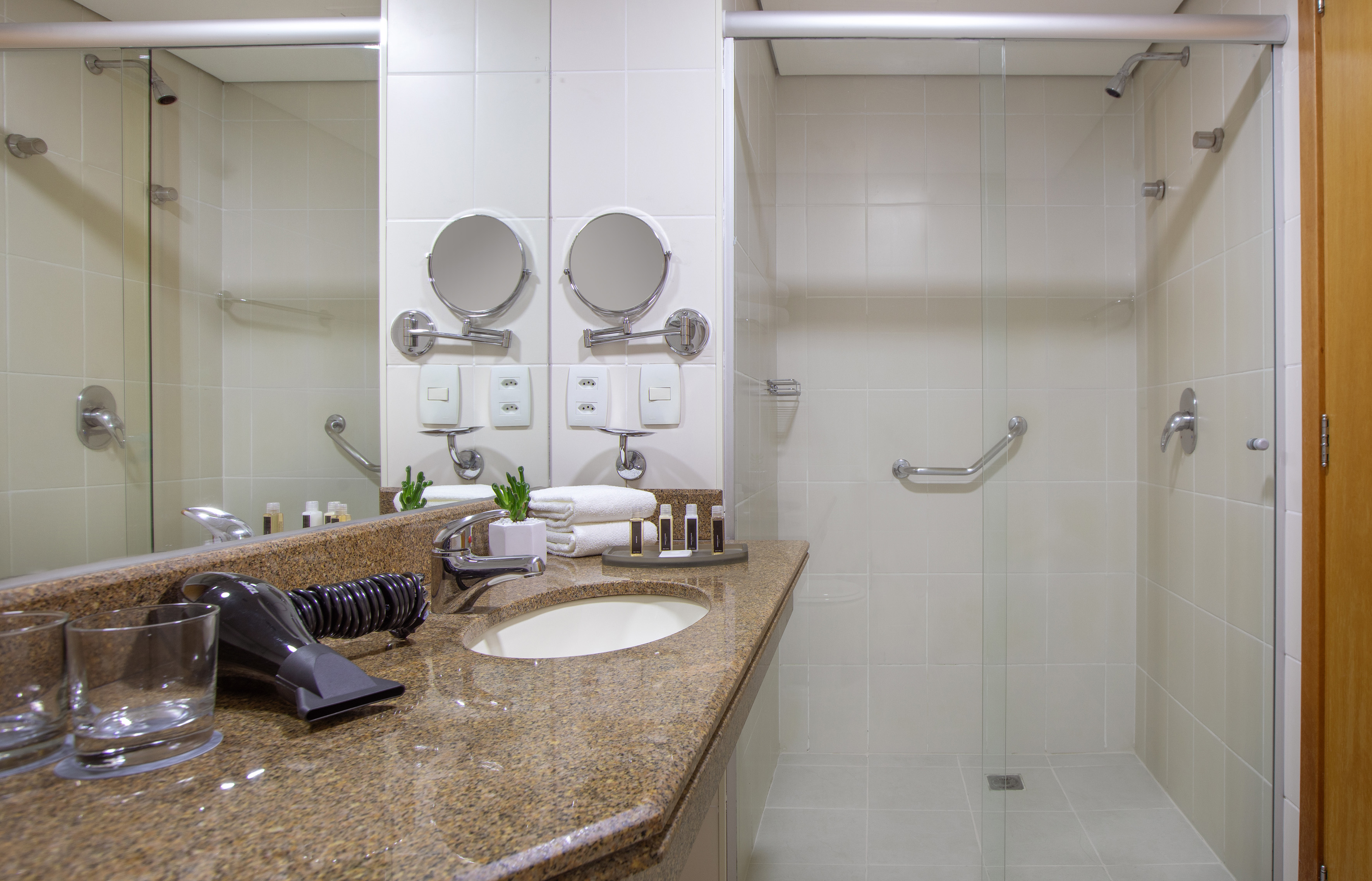 Modern hotel bathroom with granite vanity, mirror, and glass shower.