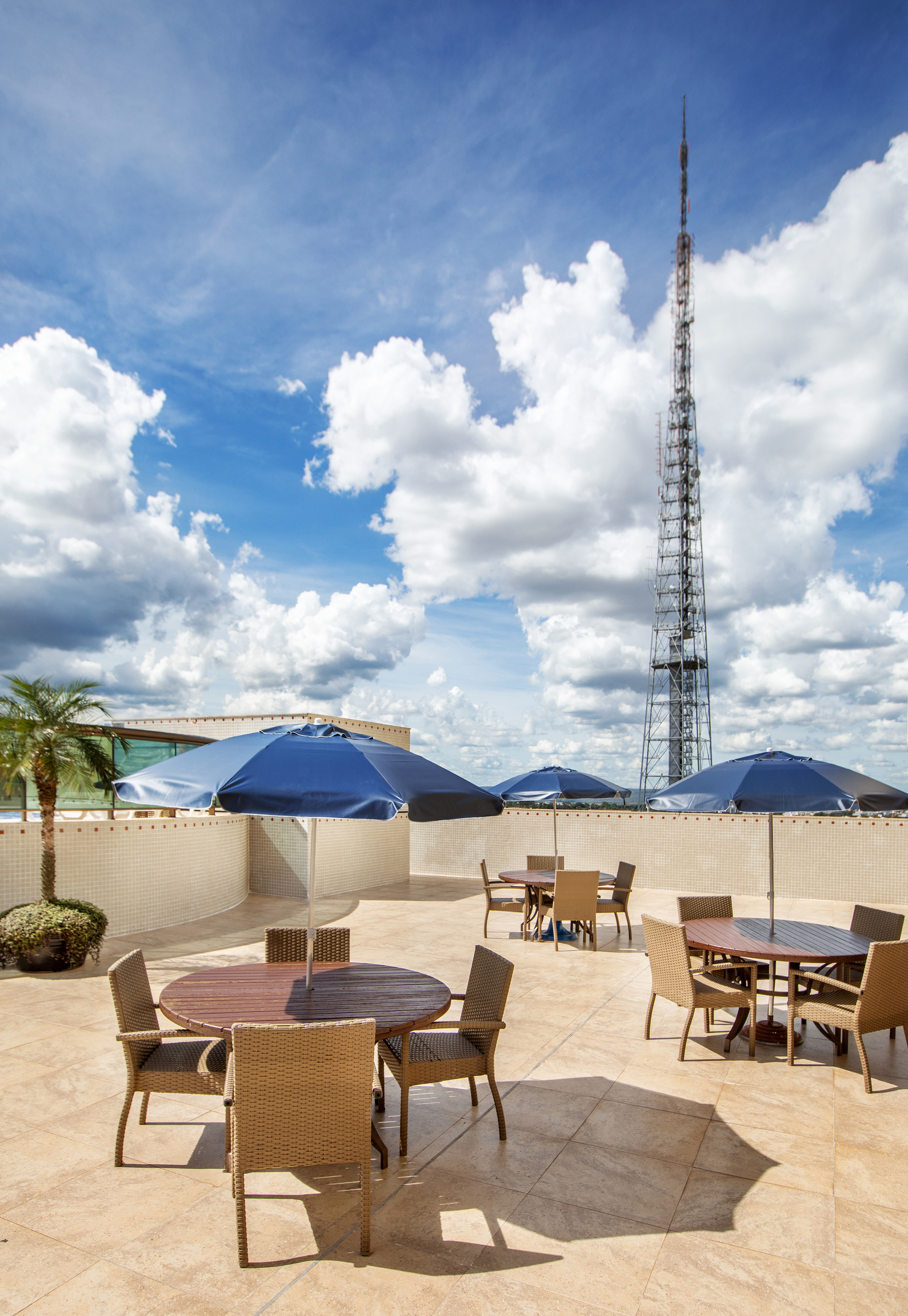Rooftop dining area with blue umbrellas, tables, and communication tower under a blue sky.