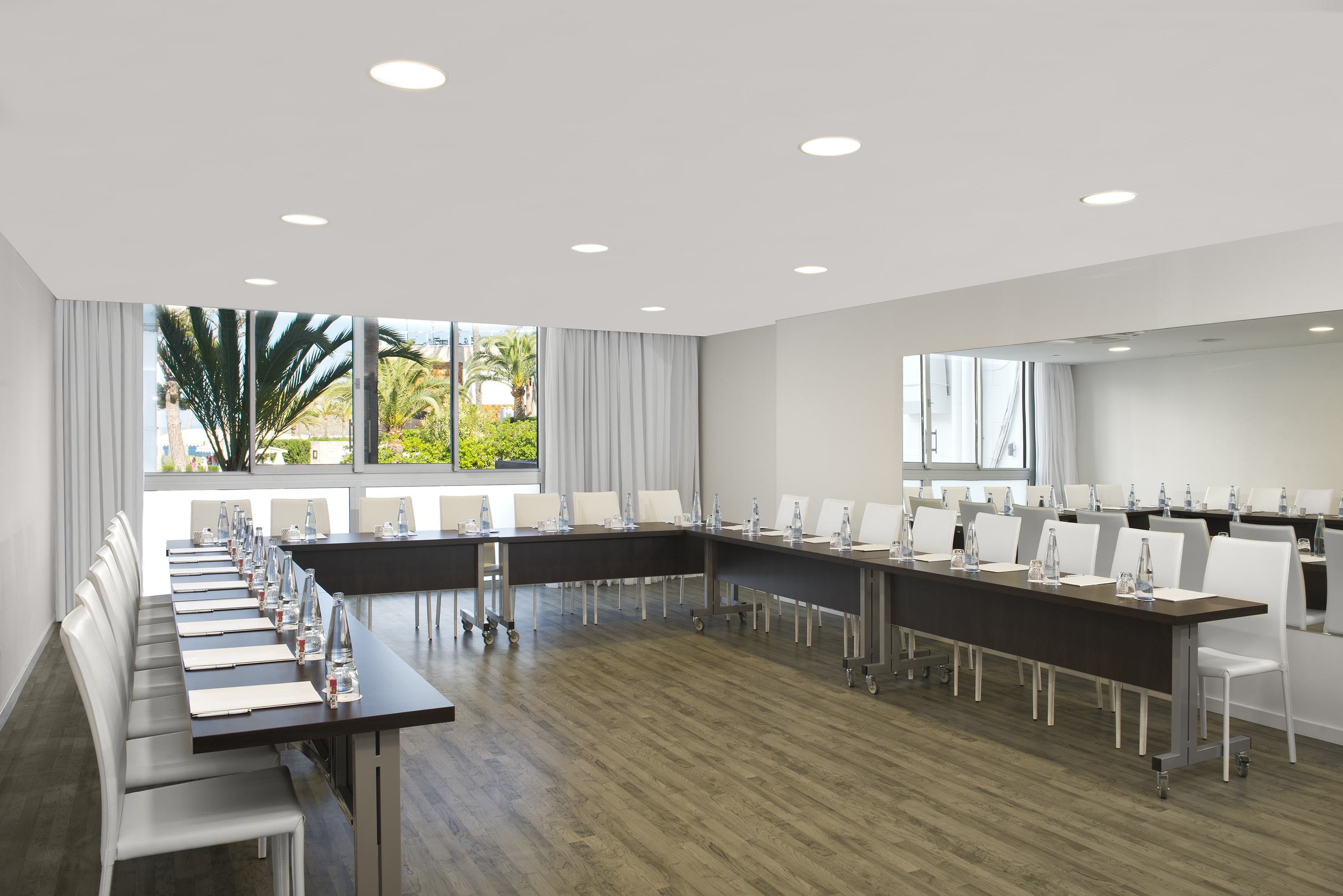 Modern U-shape conference room with white chairs and tropical window view.