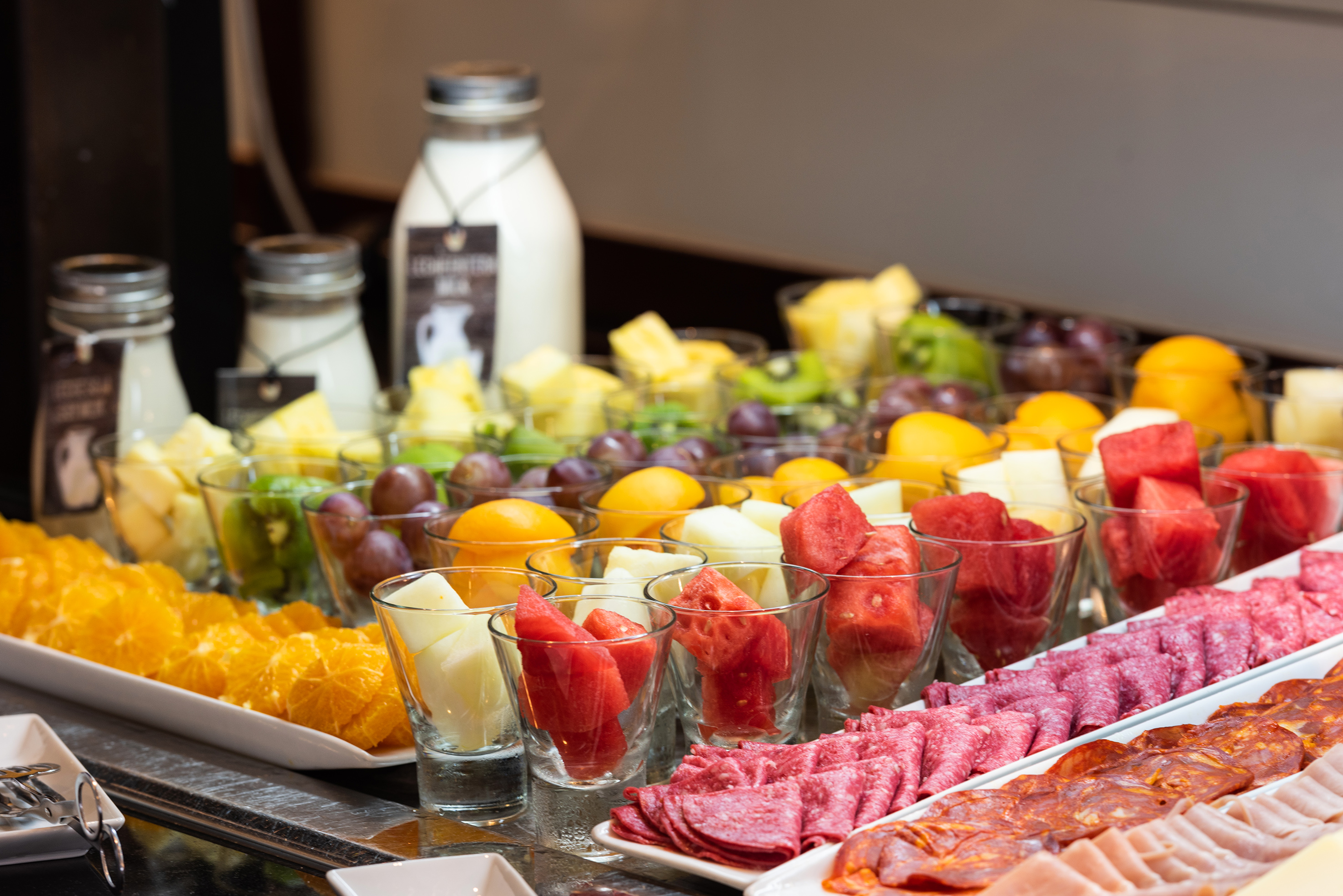 Breakfast buffet featuring fresh fruit cups, sliced oranges, and deli meats.