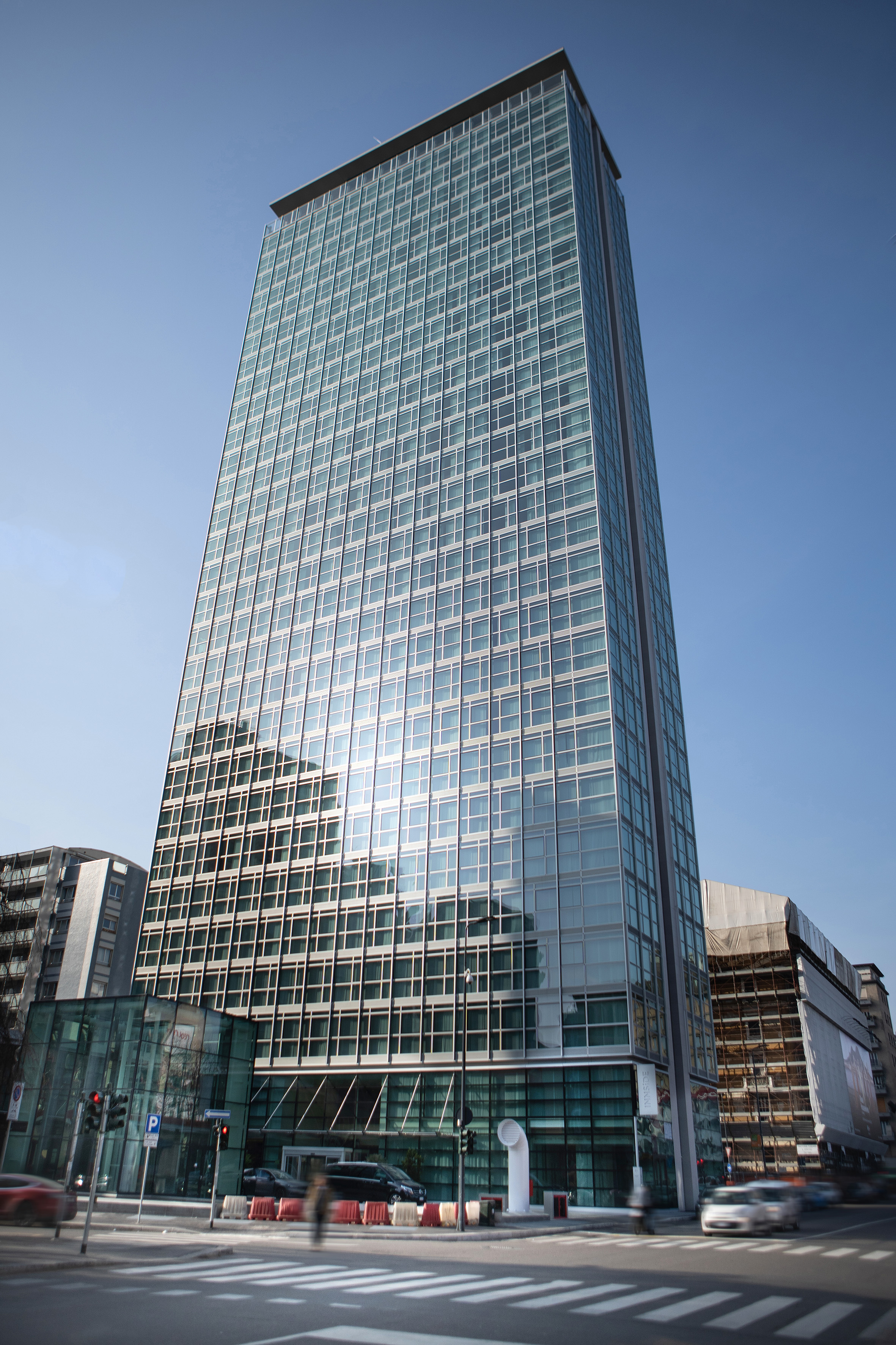 Tall glass skyscraper reflecting blue sky, with urban street below.