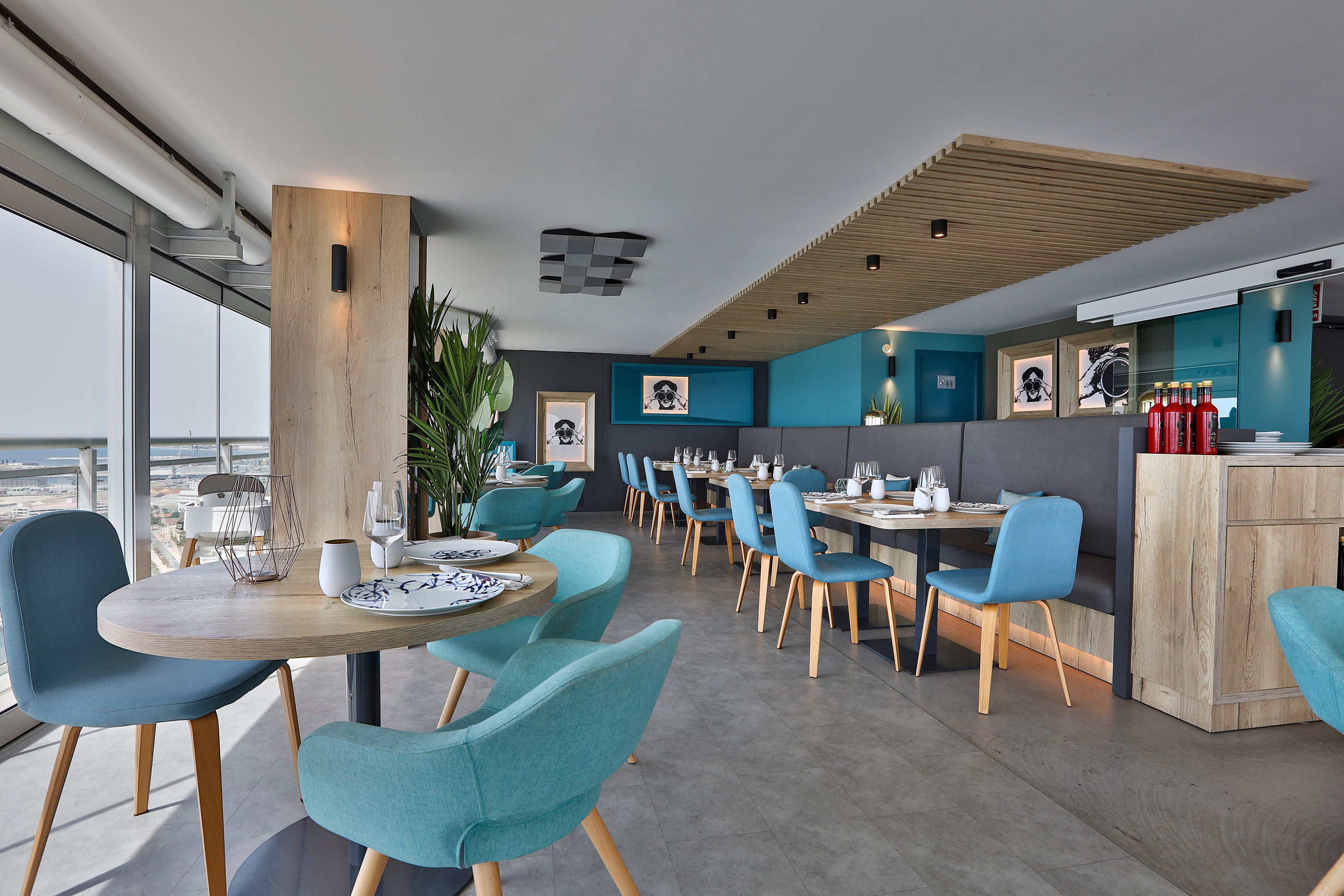 Modern restaurant interior, turquoise chairs, wooden tables, and large windows.