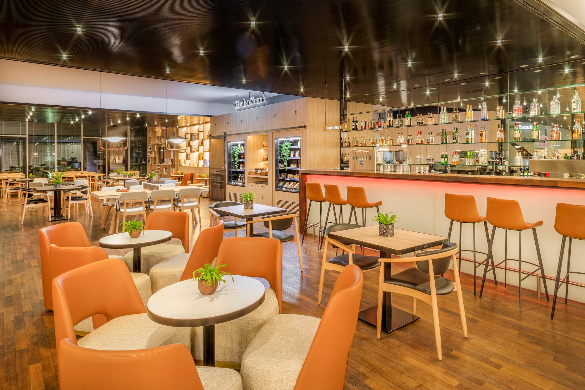 Modern lounge and bar area with orange seating, wood floors, and snack display.