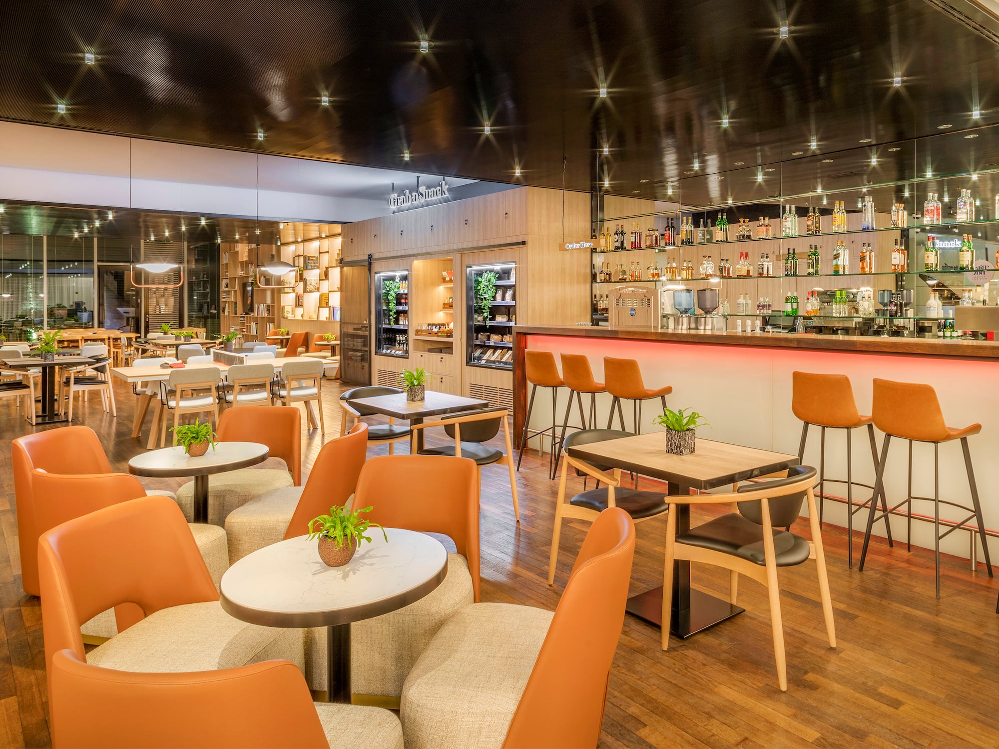 Modern restaurant bar with orange seating, snack station, and wooden floor.