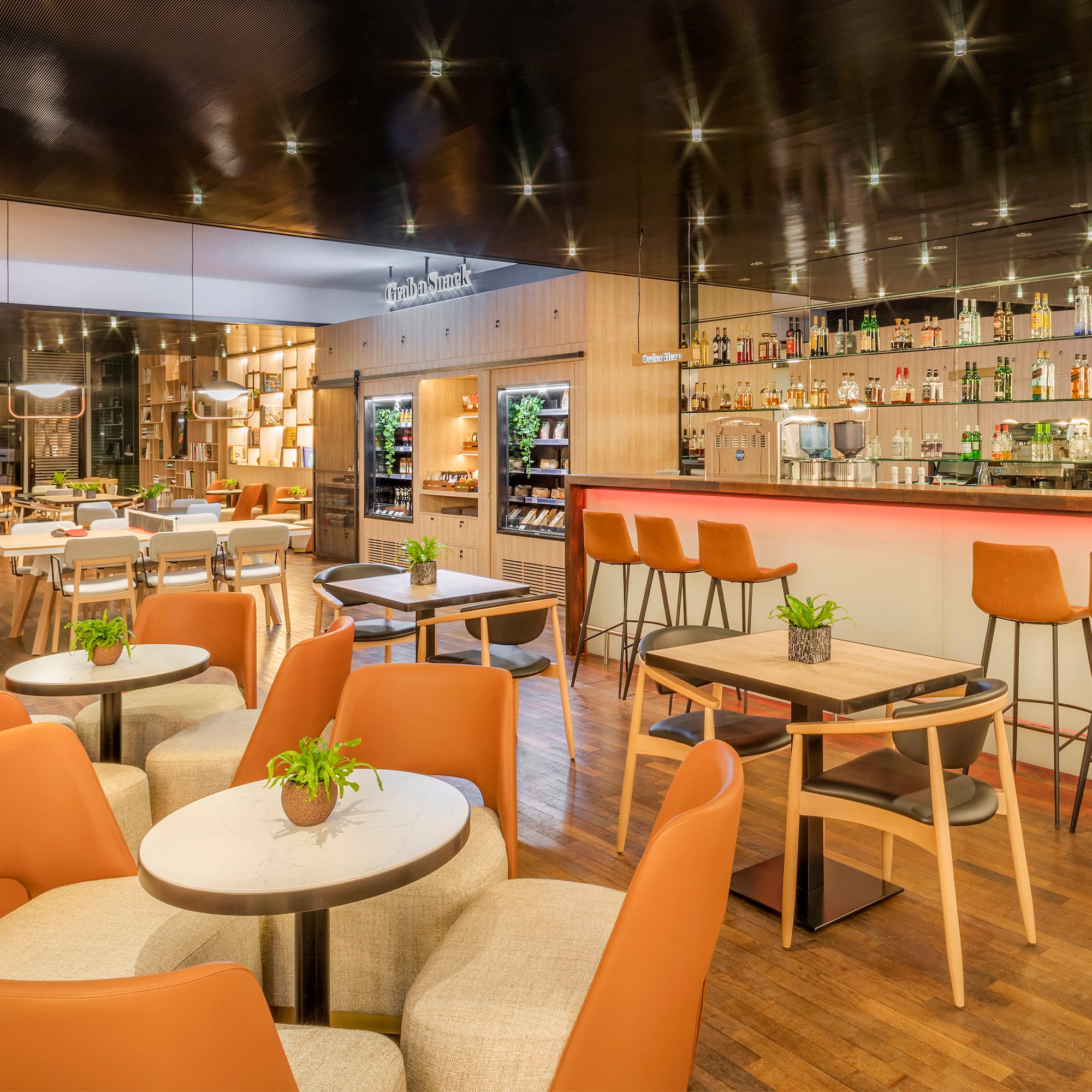 Modern restaurant bar with orange seating, snack station, and wooden floor.