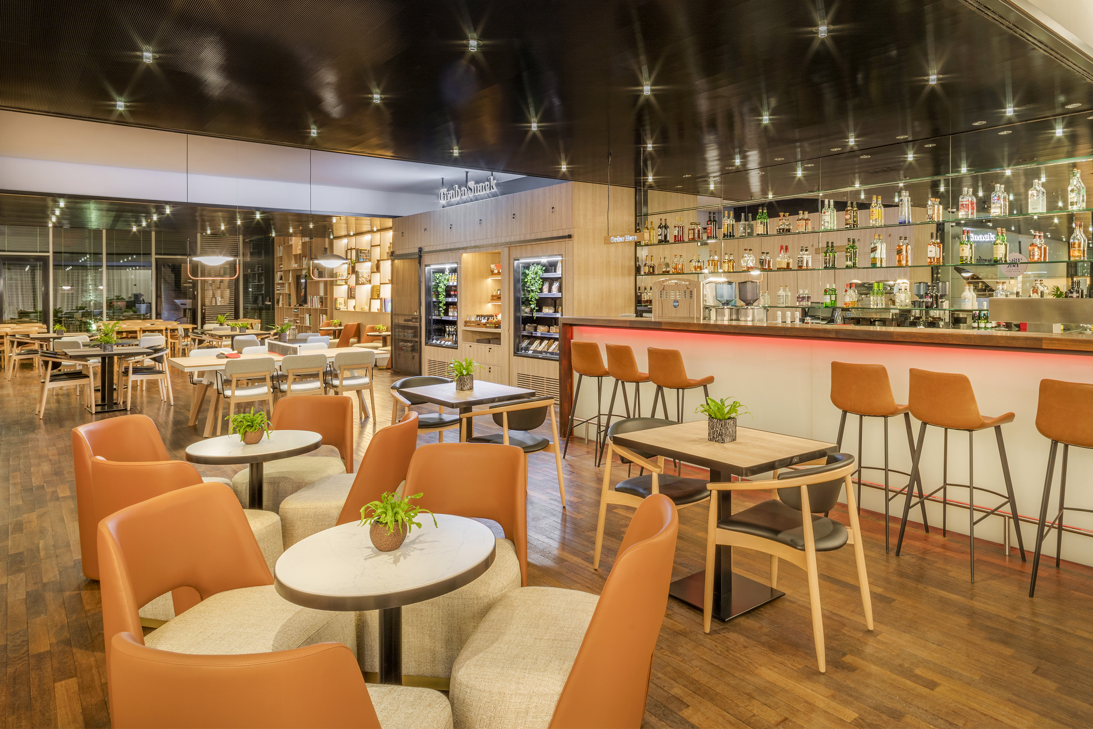Modern restaurant bar with orange seating, snack station, and wooden floor.