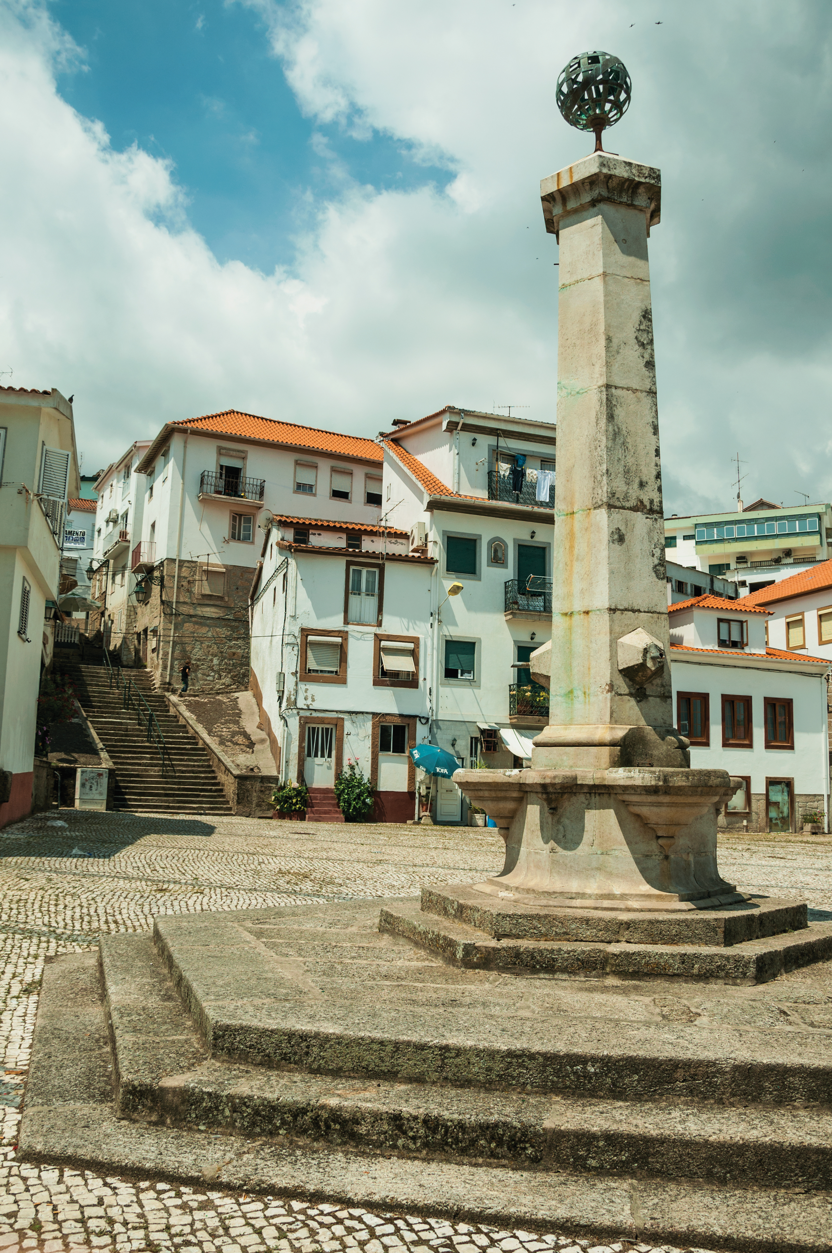 a stone pillar in a courtyard with buildings in the background