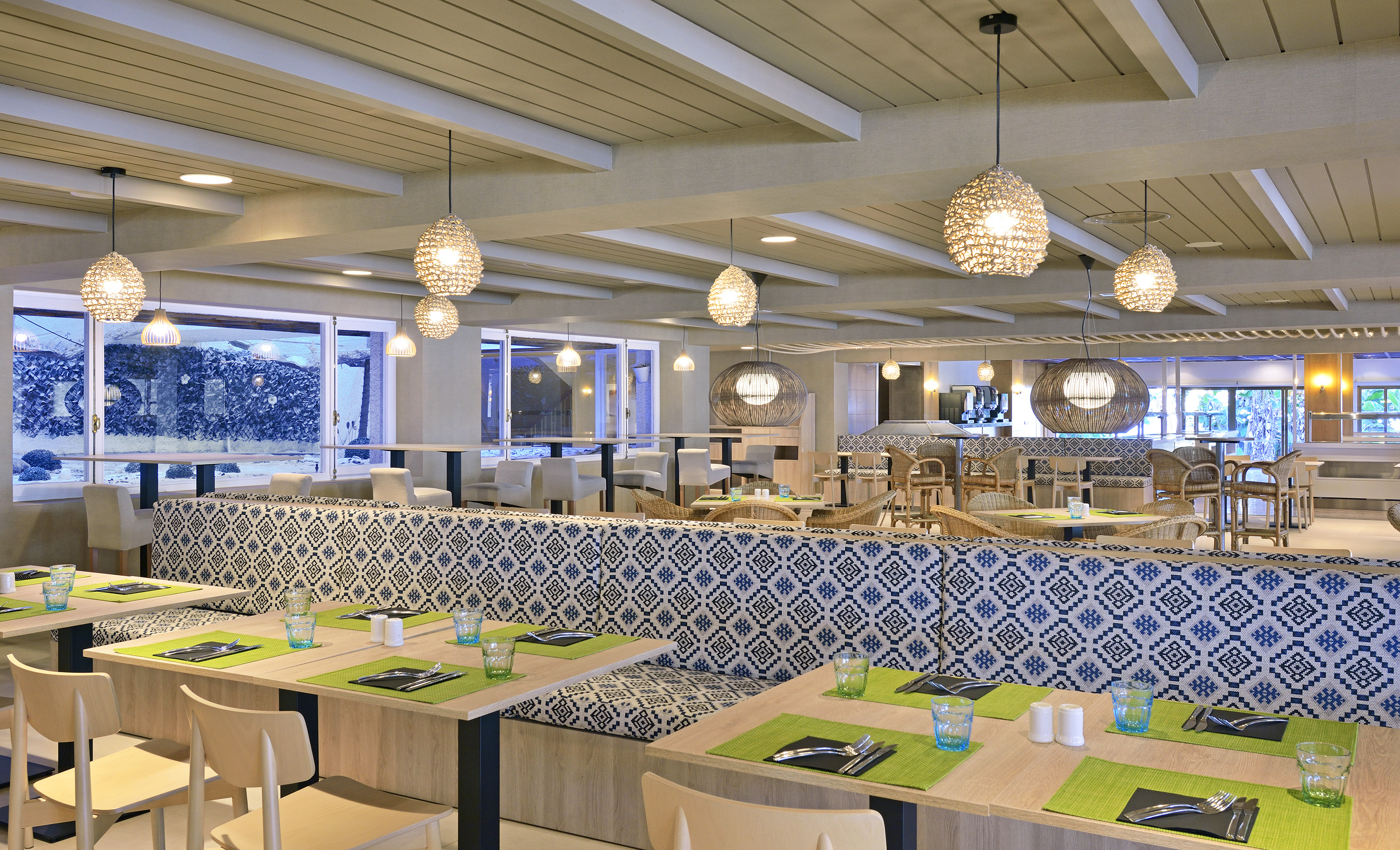 Bright dining area with patterned banquettes, light wood tables, woven lights.