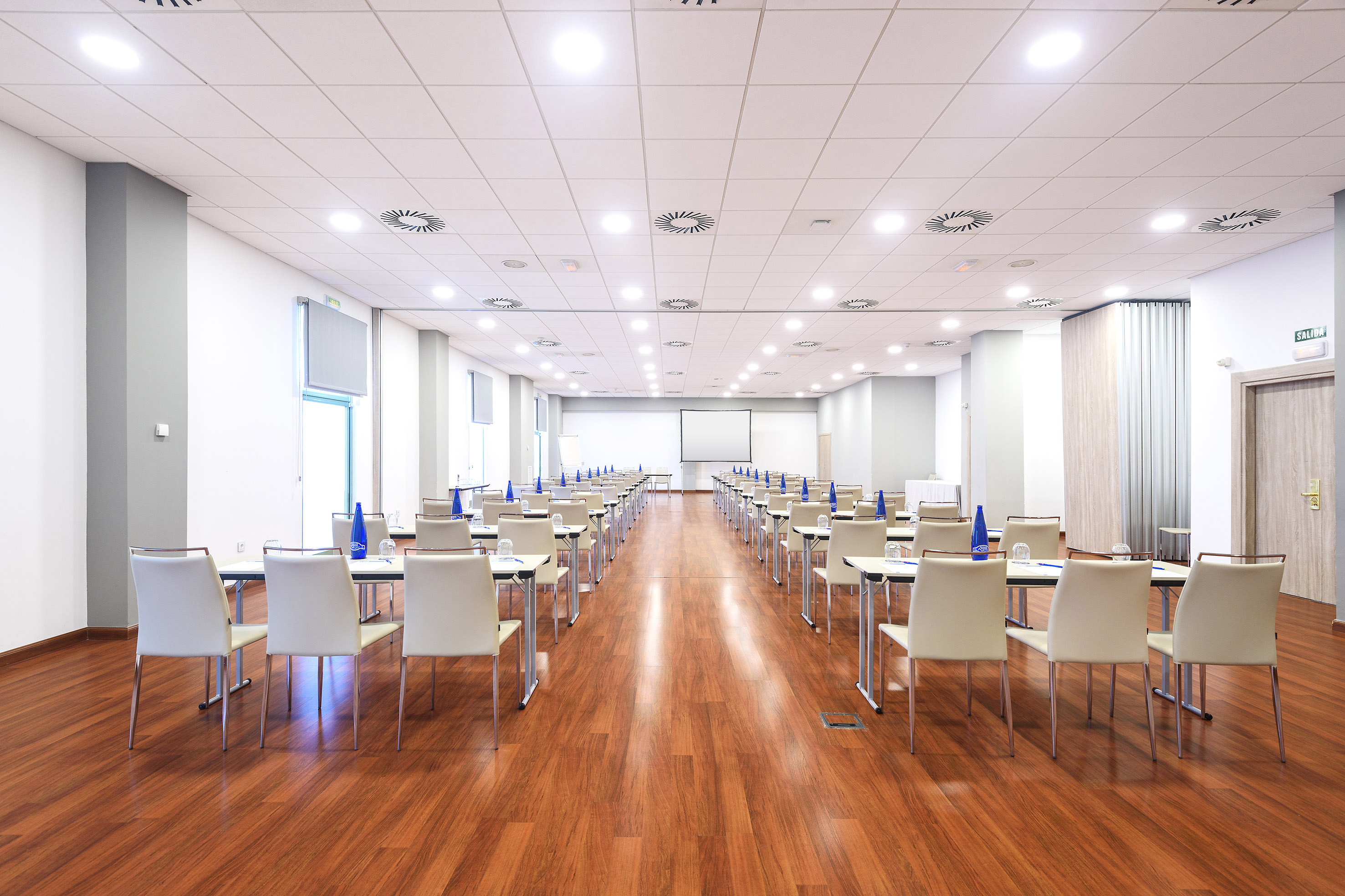 Empty conference room with rows of tables, chairs, projector, and wood floor.