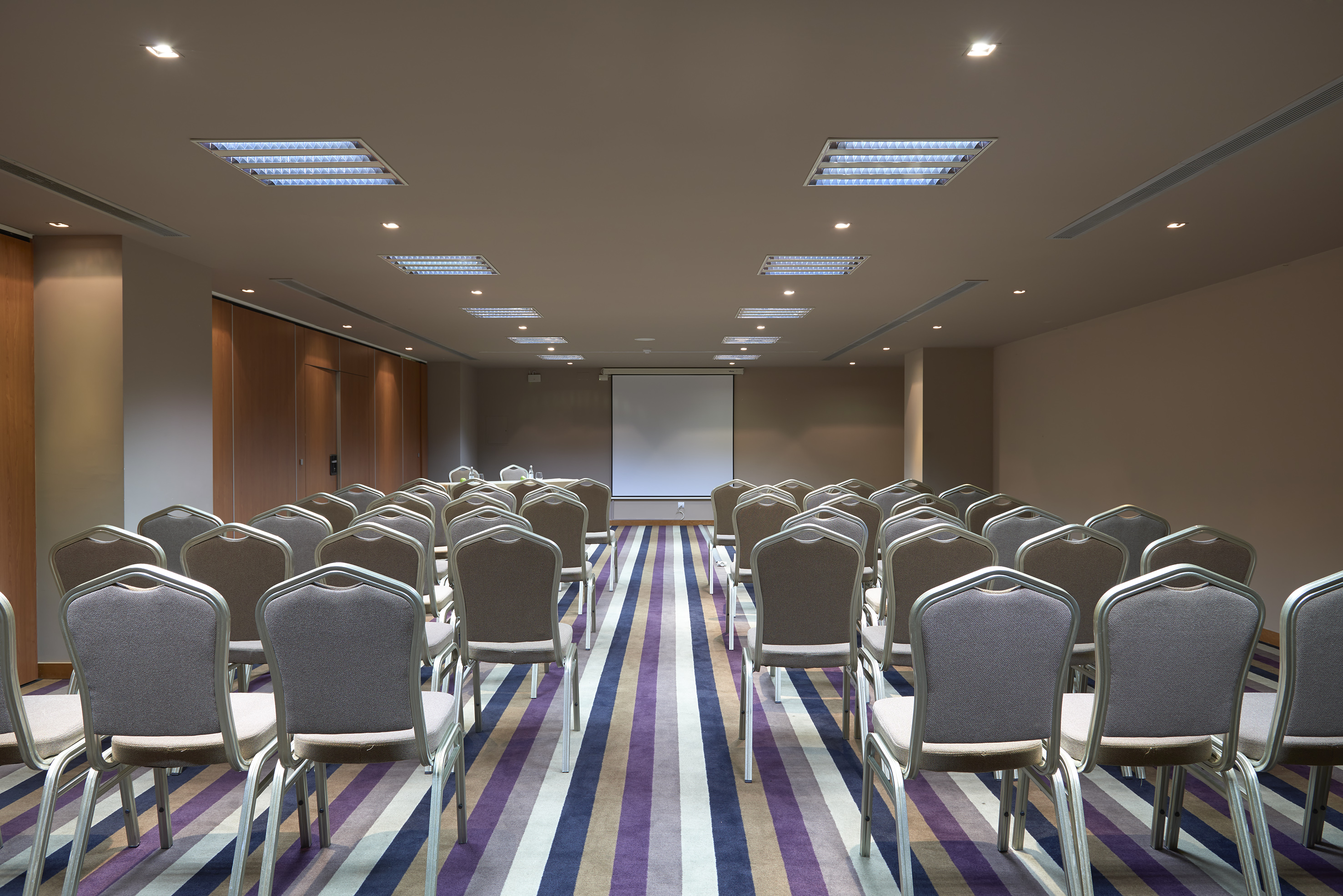 Empty conference room with gray chairs, projector screen, and striped purple carpet.