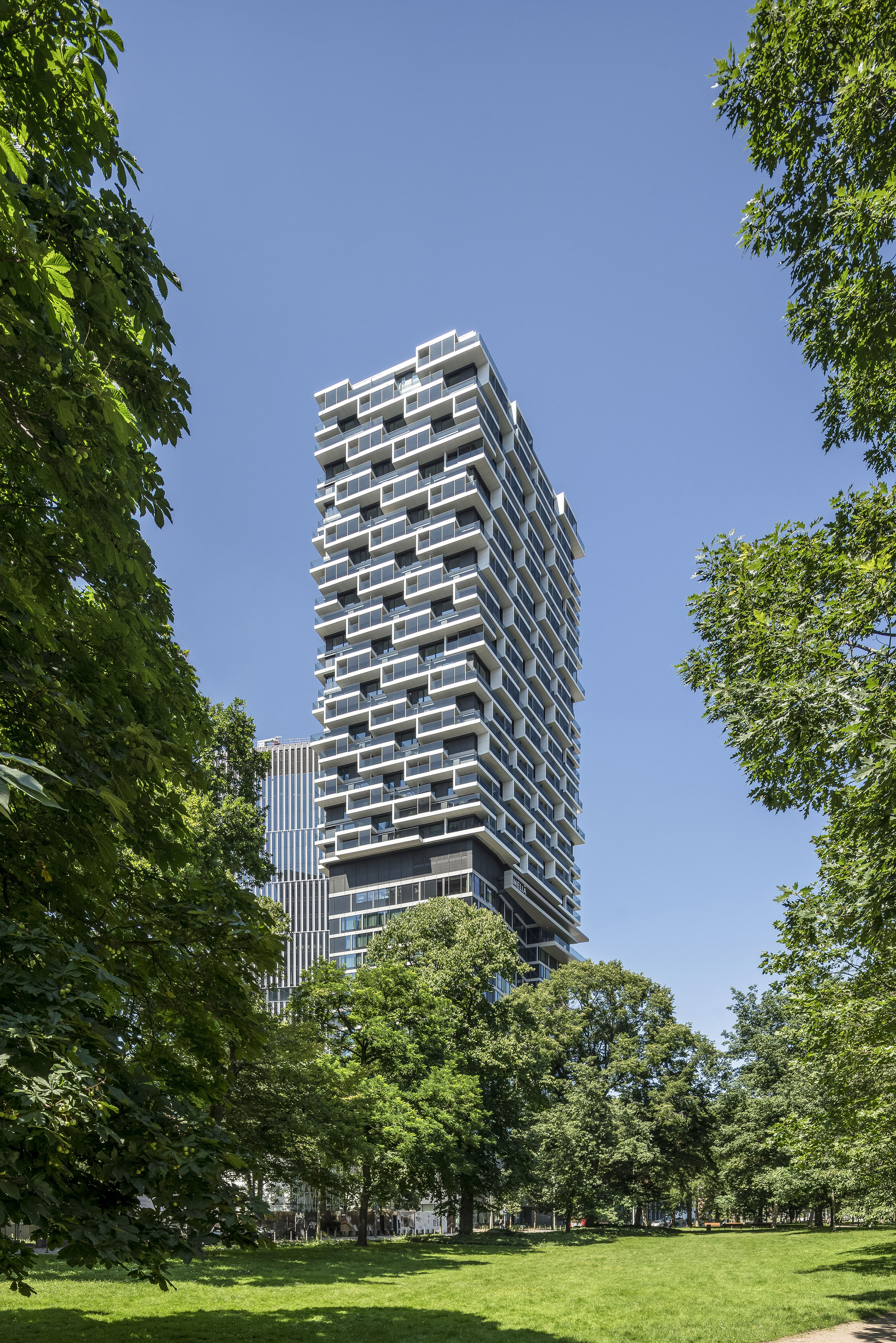 Meliá hotel, modern high-rise with white balconies, framed by green park trees.