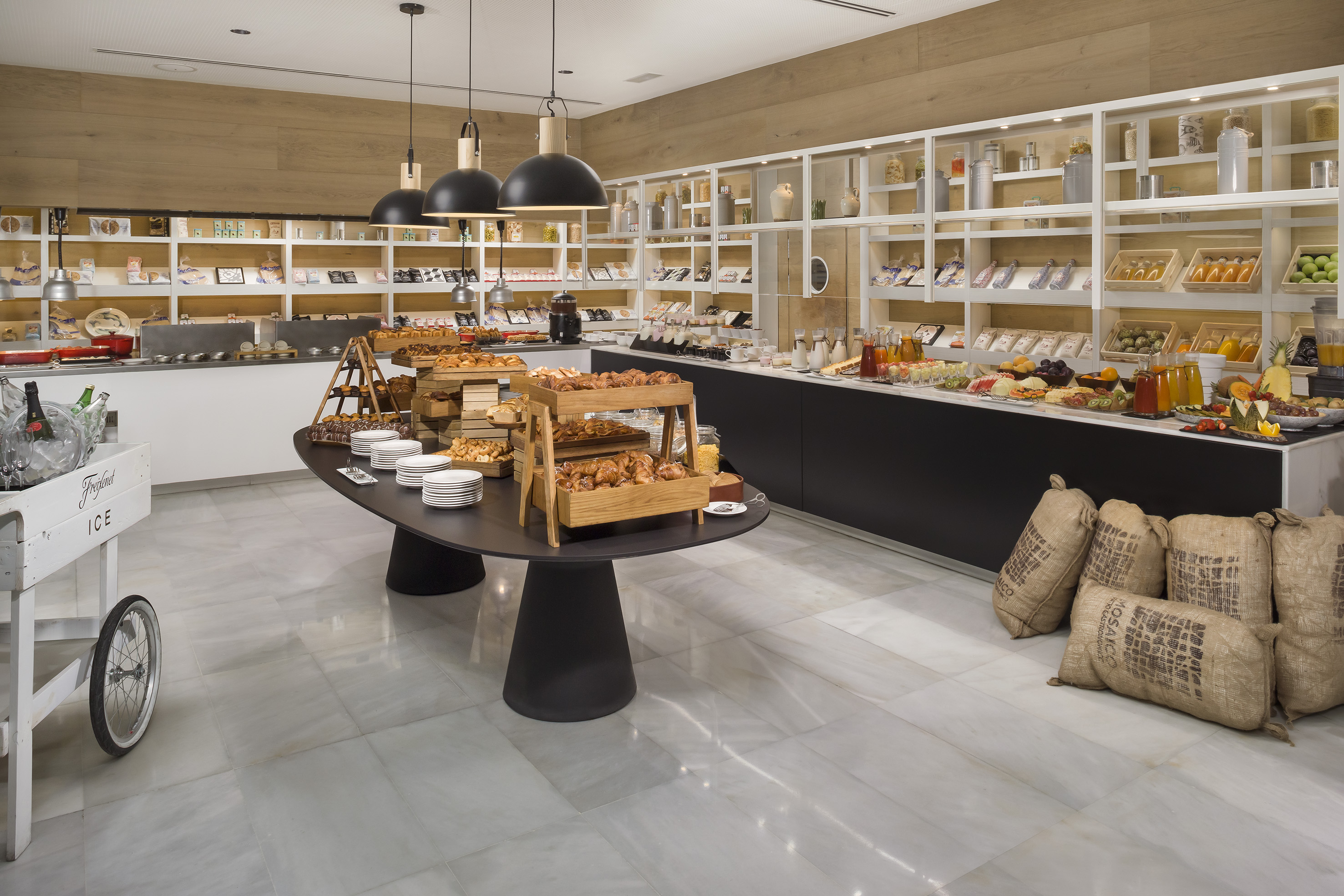 Modern hotel breakfast buffet with pastries, fruits, and juices on display.