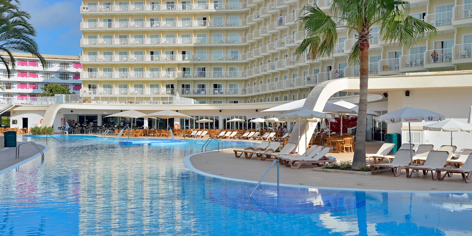 a pool with lounge chairs and umbrellas in front of a large building