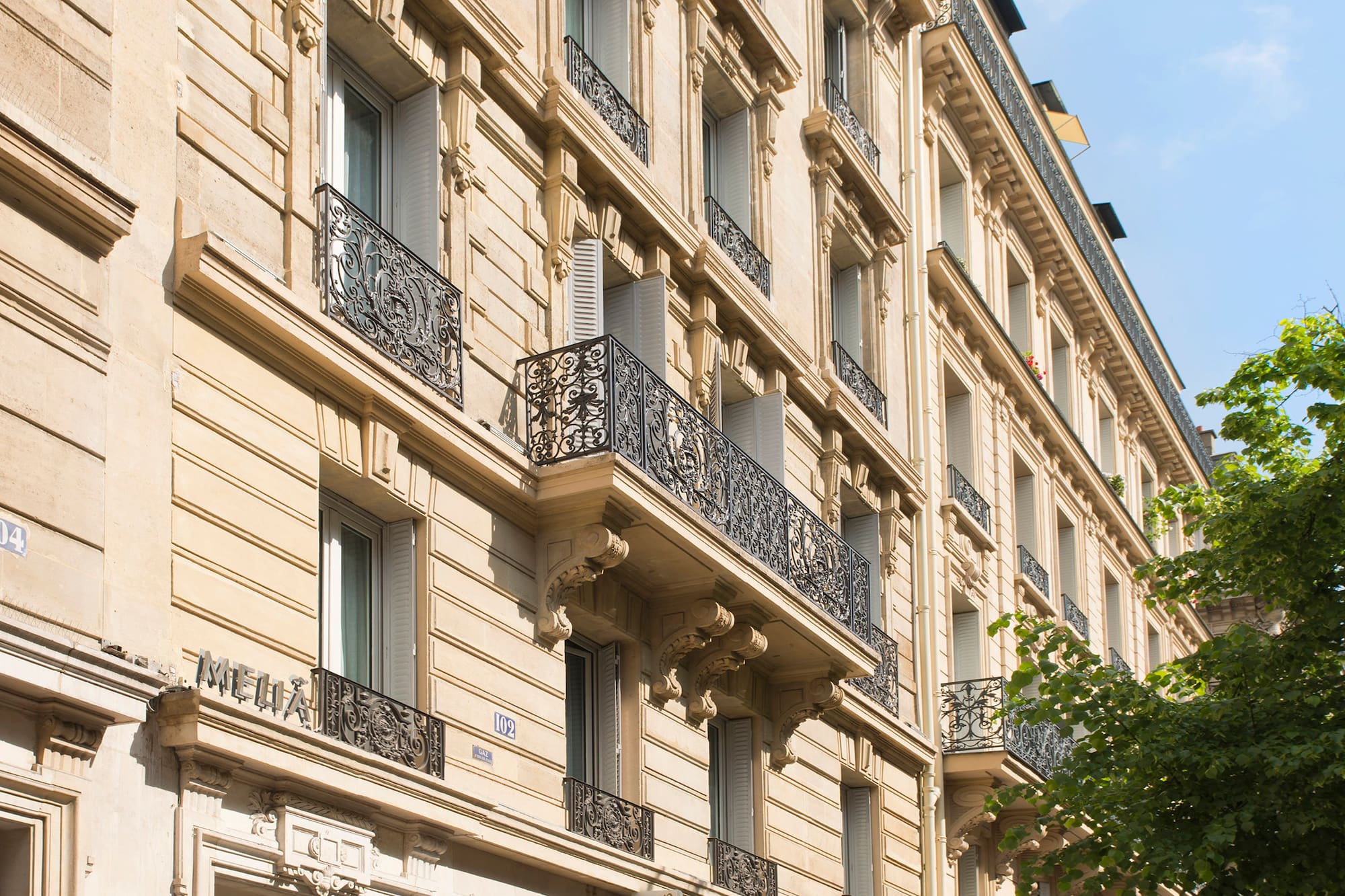 Haussmannian Parisian building with ornate balconies, Melia hotel, and street shops.