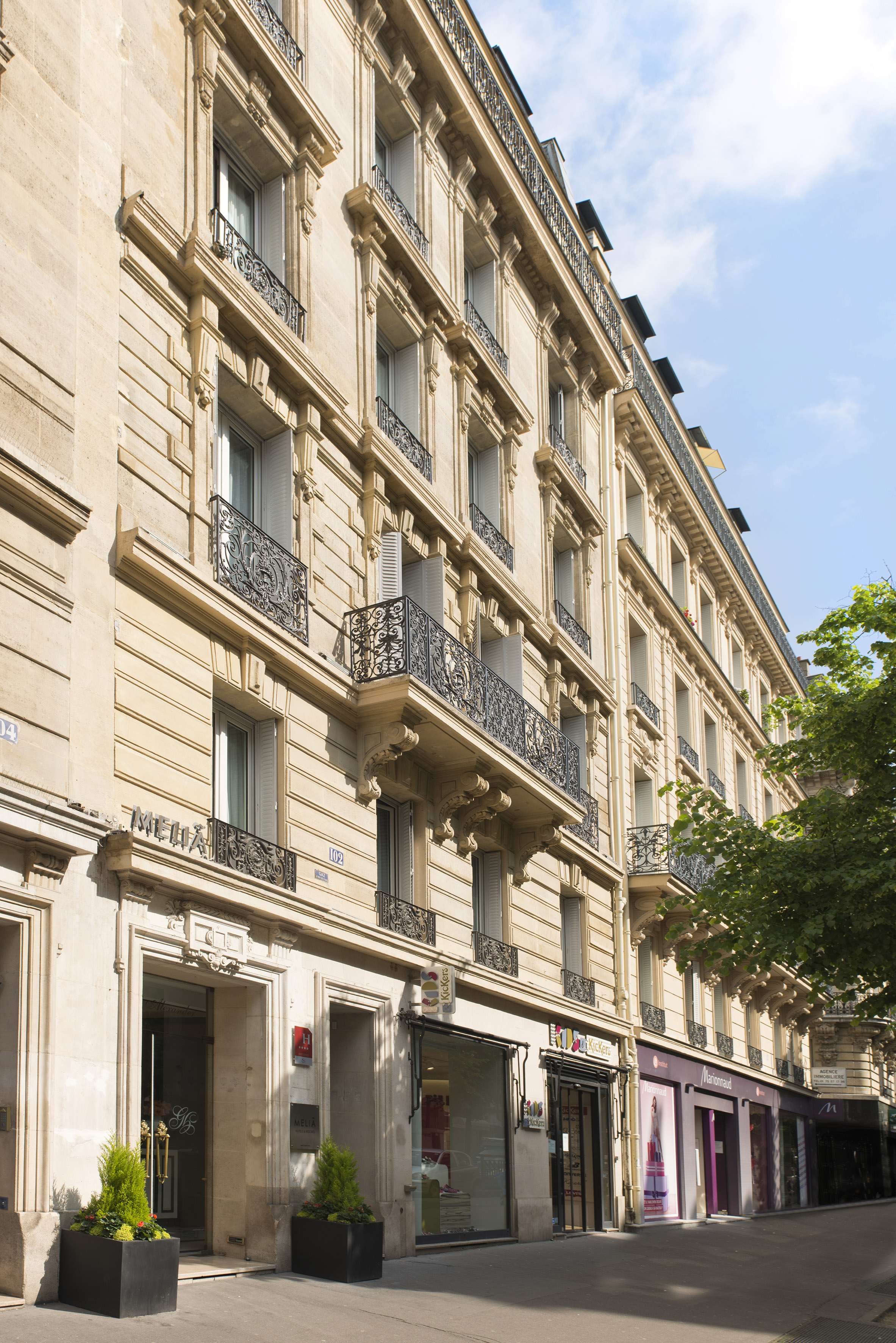 Haussmannian Parisian building with ornate balconies, Melia hotel, and street shops.