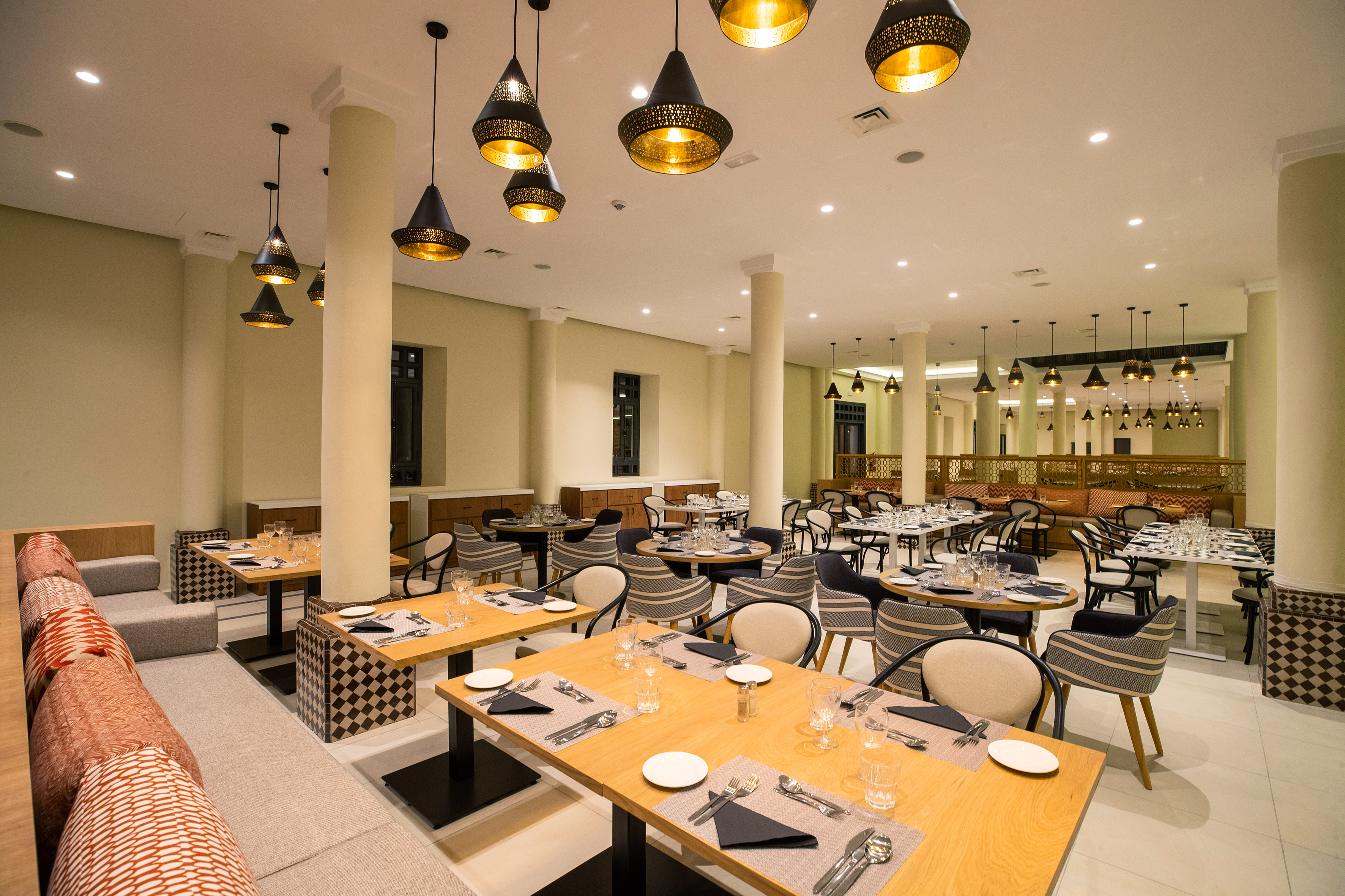 Elegant Moroccan restaurant dining room with set tables, modern chairs, and pendant lights.