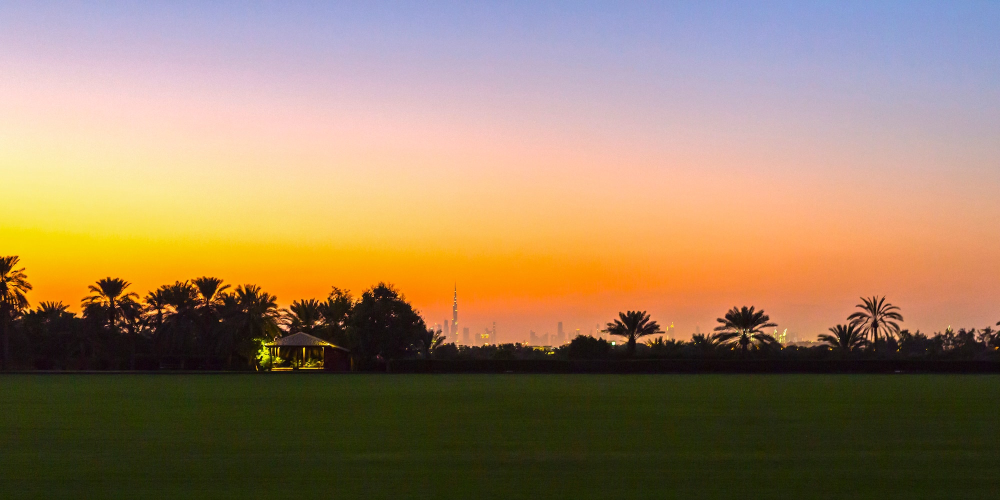 a sunset over a large green field with trees and a building in the distance