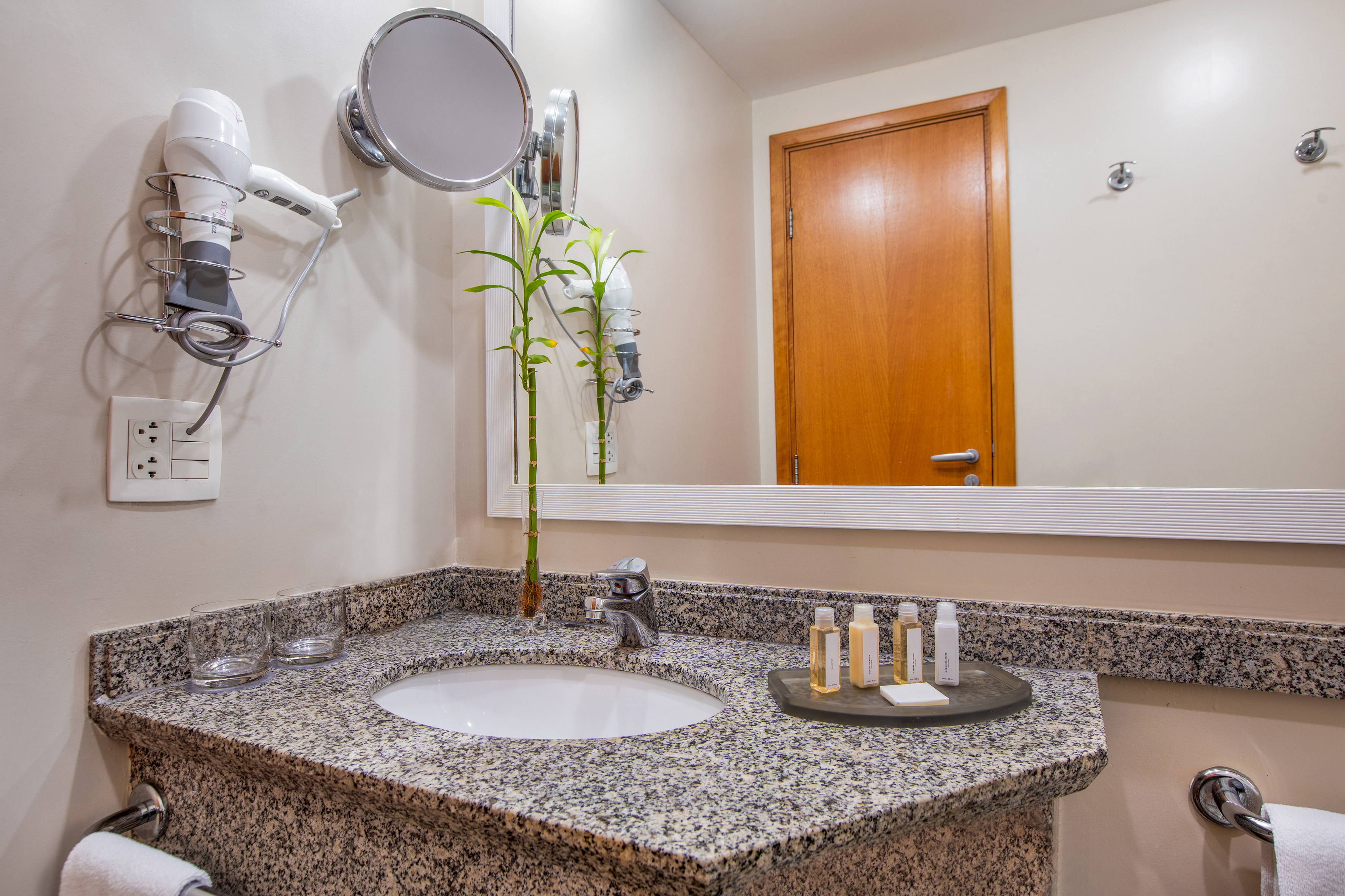 Hotel bathroom vanity, granite countertop, sink, mirror, hairdryer, and toiletries.