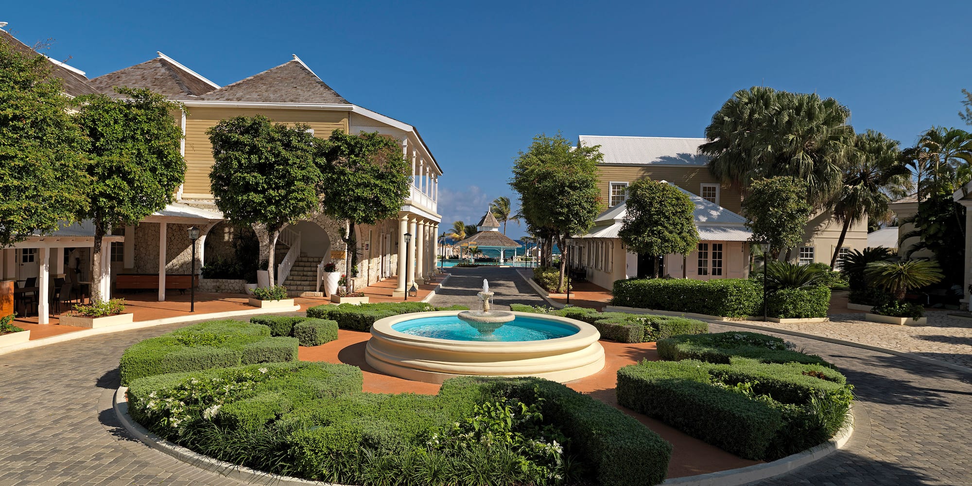 a fountain in a circle with bushes and buildings in the background
