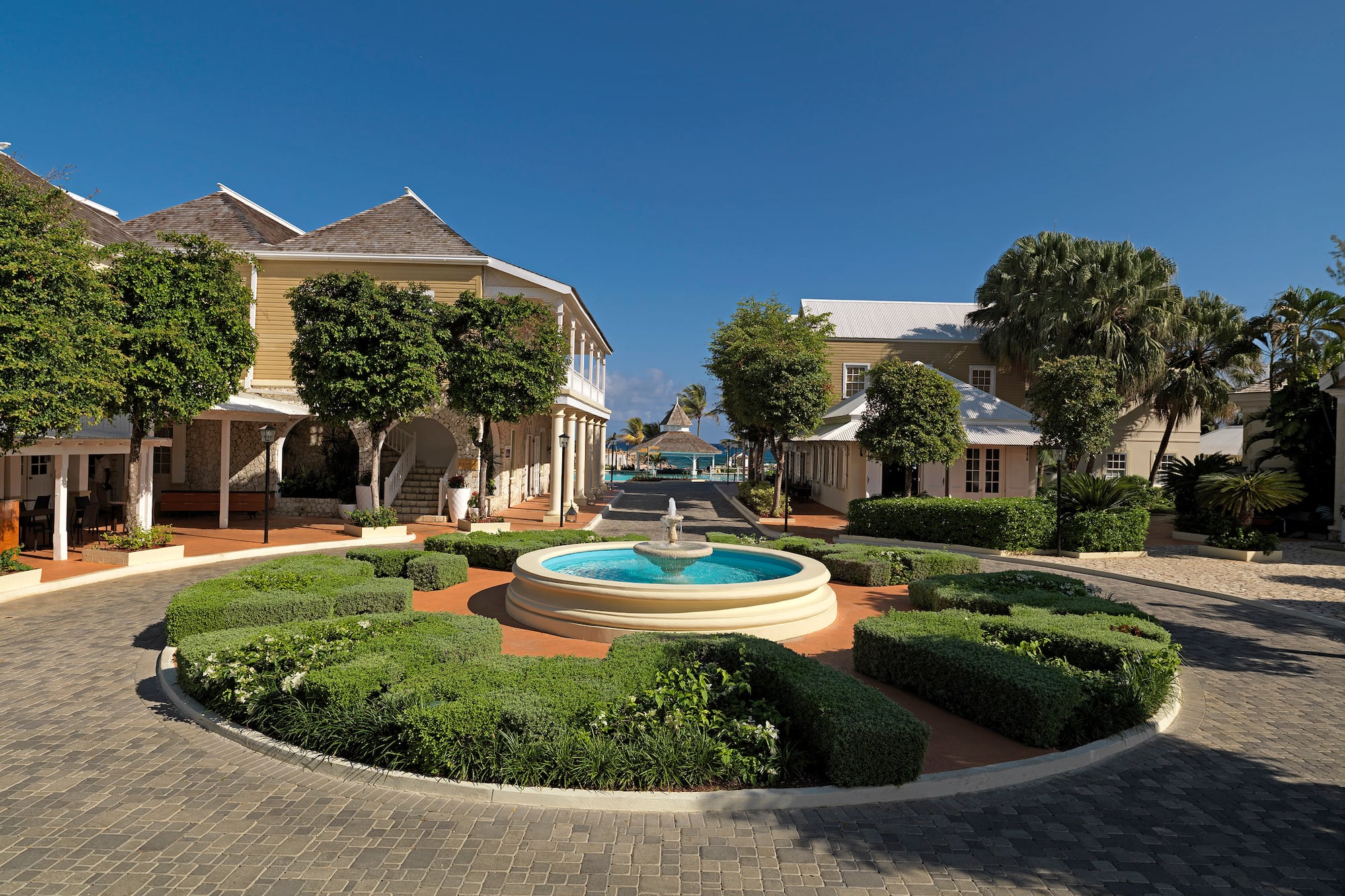 a fountain in a circle with bushes and buildings in the background