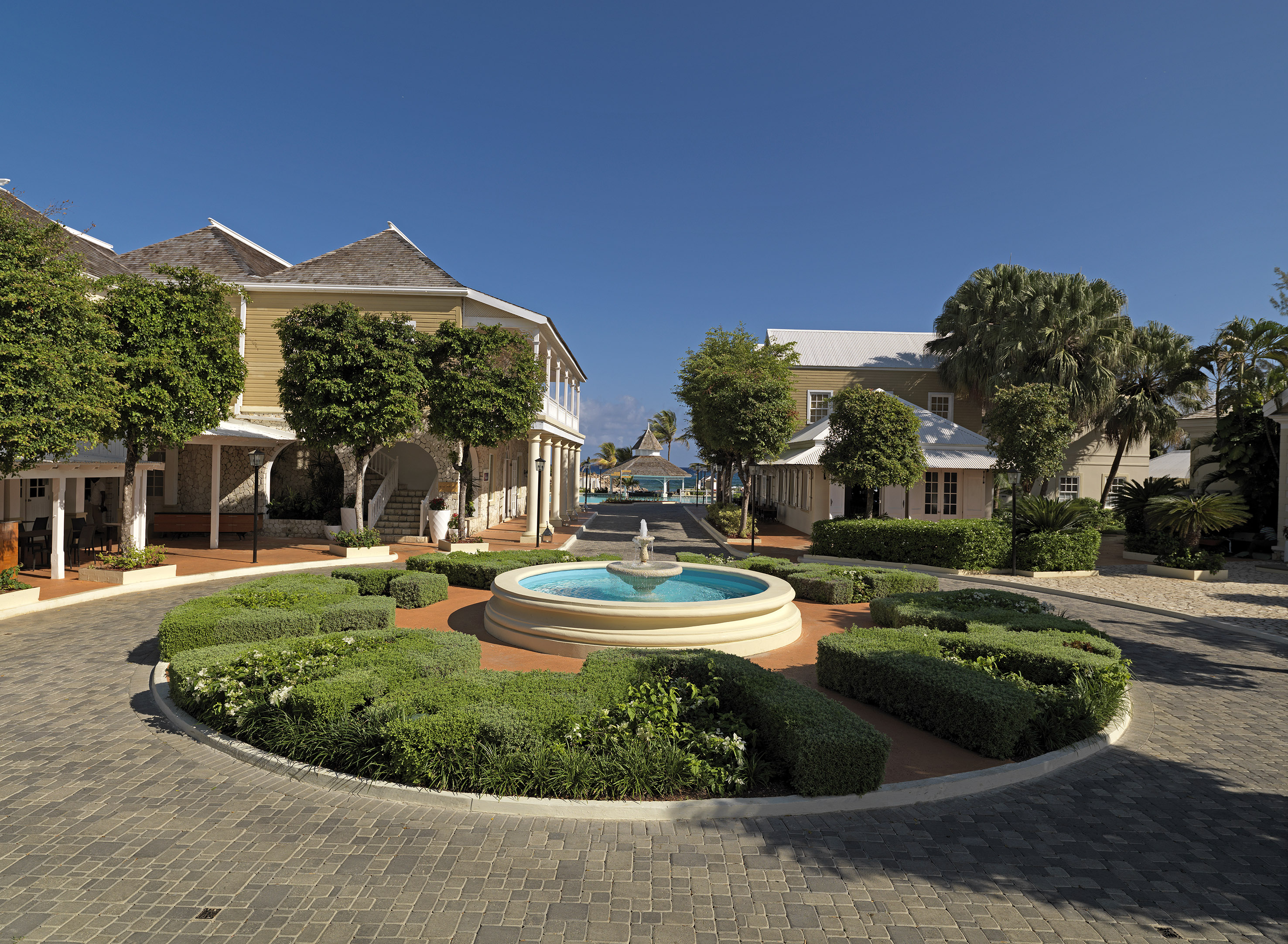 a fountain in a circle with bushes and buildings in the background