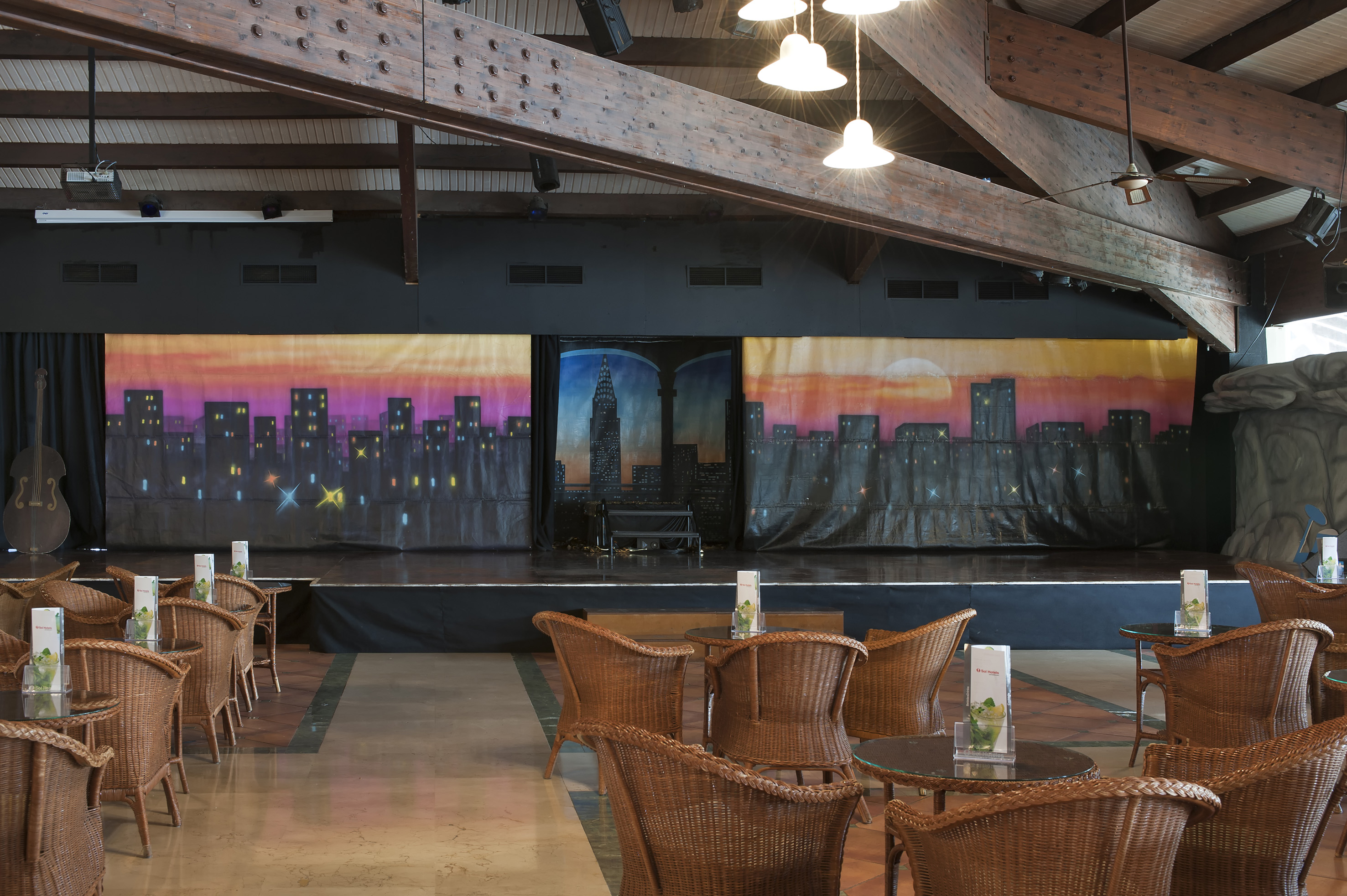 Resort entertainment lounge with cityscape stage backdrop and wicker chairs.